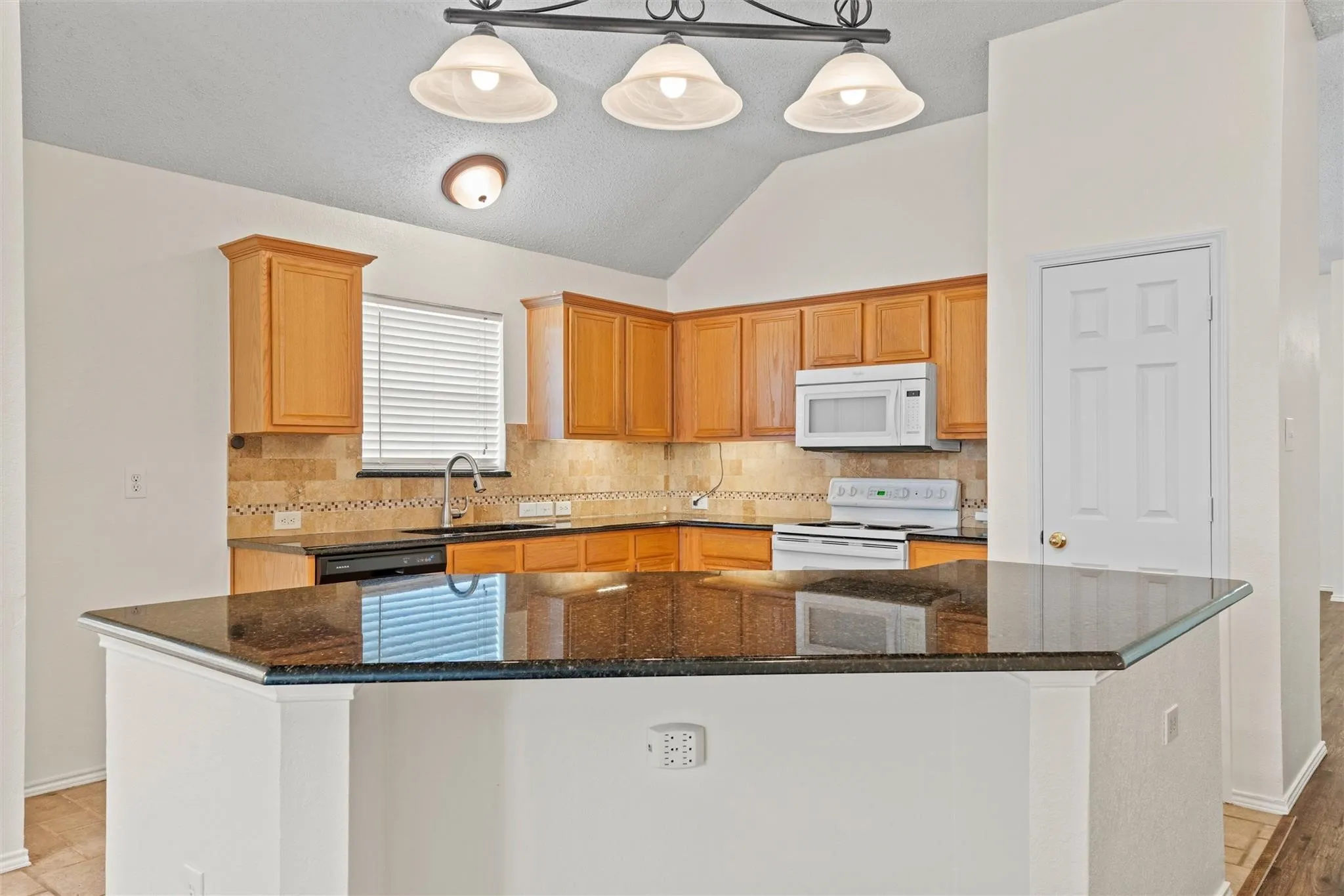 Kitchen featuring wood cabinetry, dark countertops, a tiled backsplash, white appliances, and vaulted ceilings