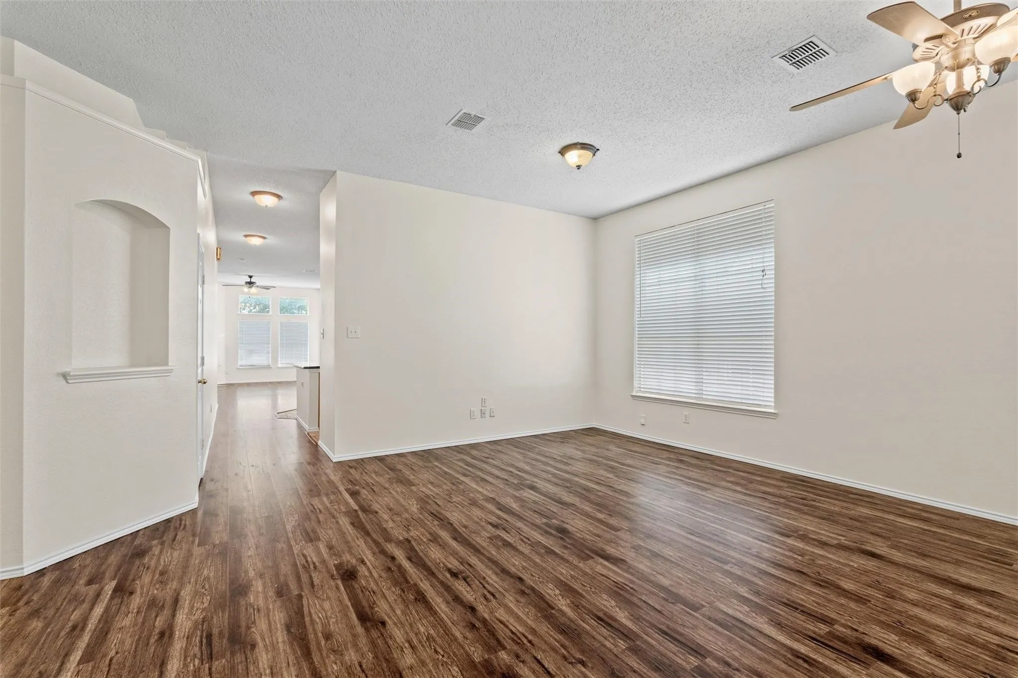Wood-finish flooring throughout, ceiling fan with integrated lighting, recessed wall niche, window with horizontal blinds, and a neutral color palette