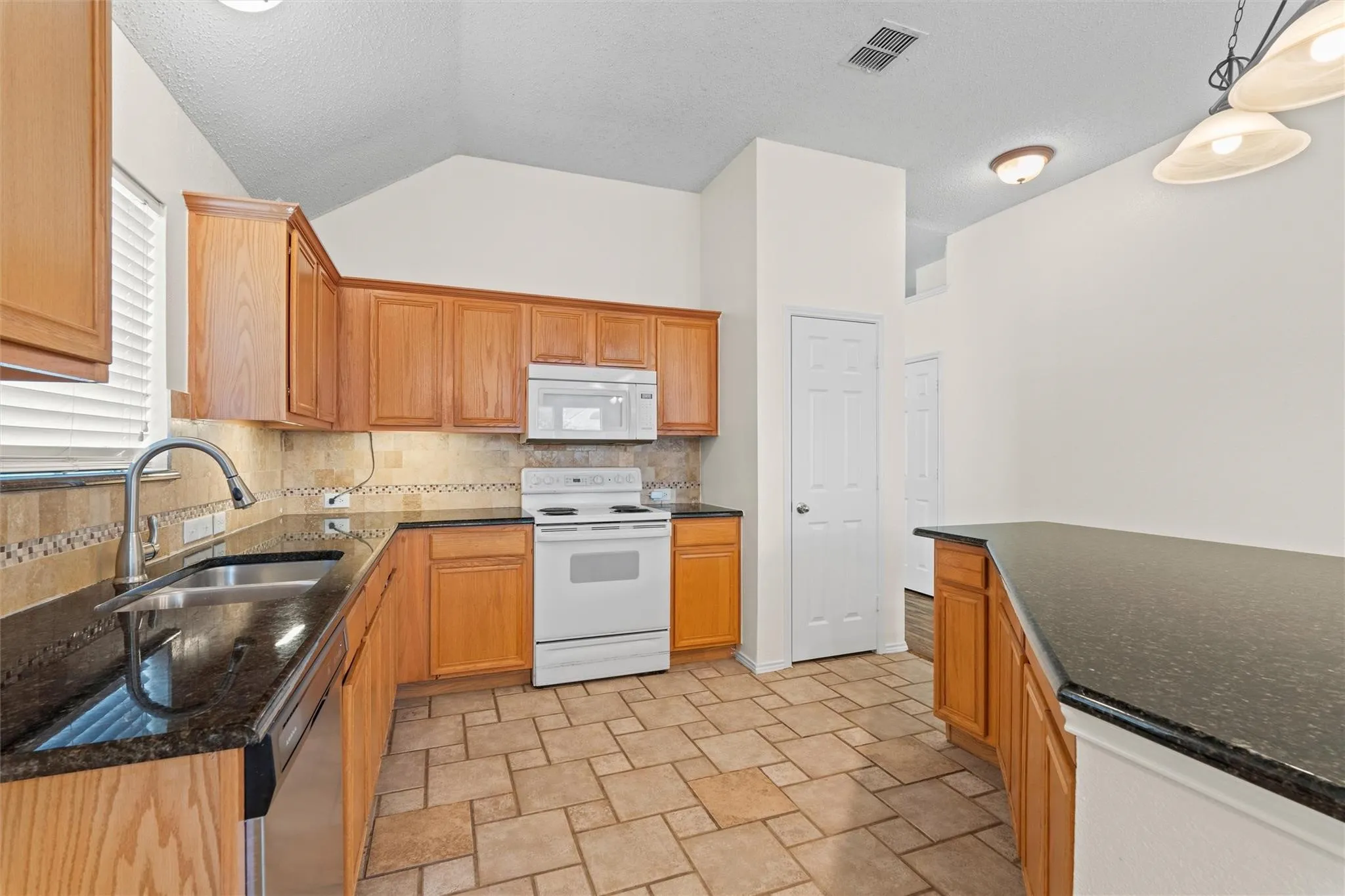 Kitchen featuring wood cabinetry, dark countertops, a tile backsplash, stainless steel sink, and tile flooring