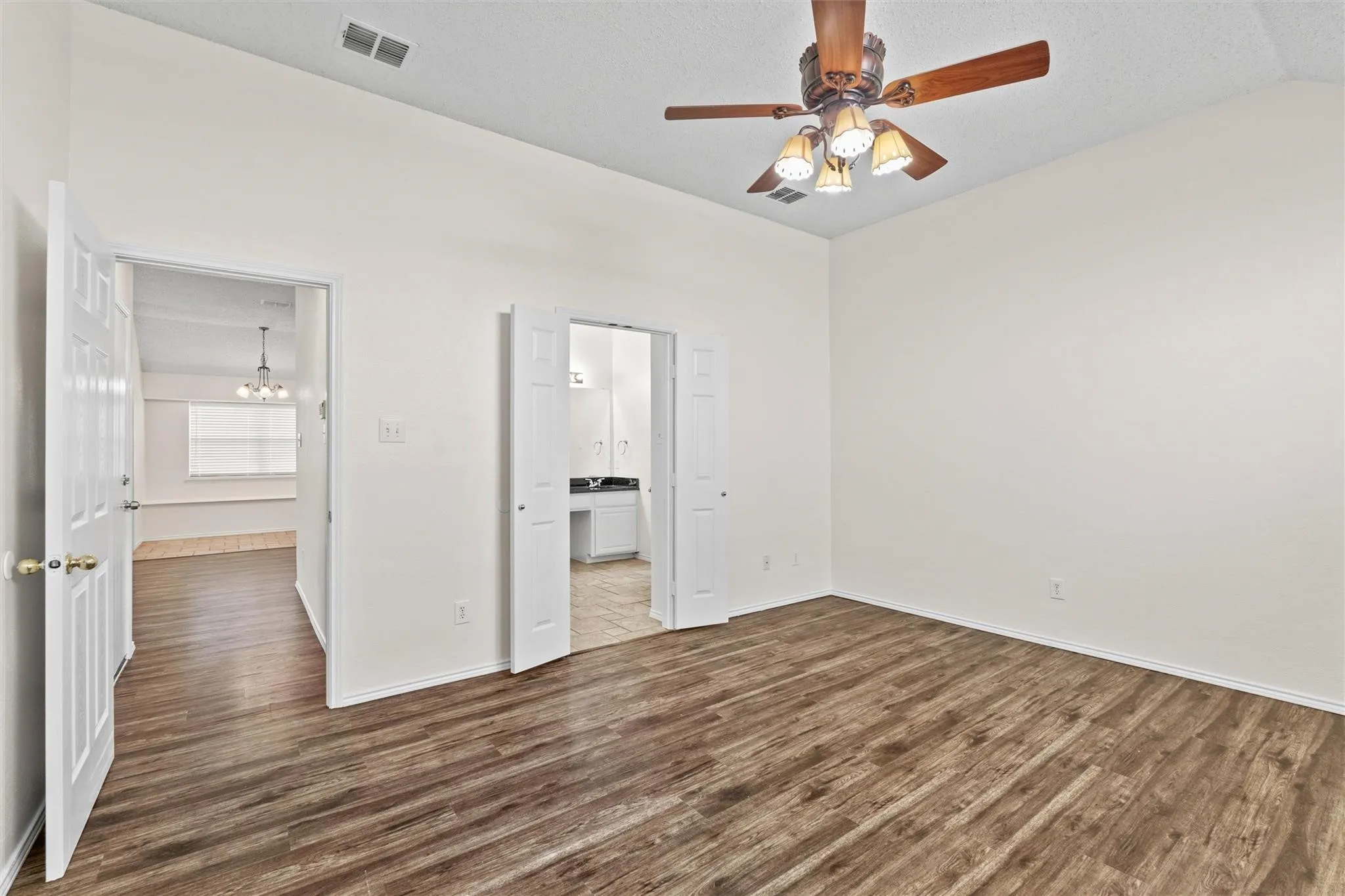 Vaulted ceiling, wood-finish flooring, ceiling fan with light fixture, and white interior doors