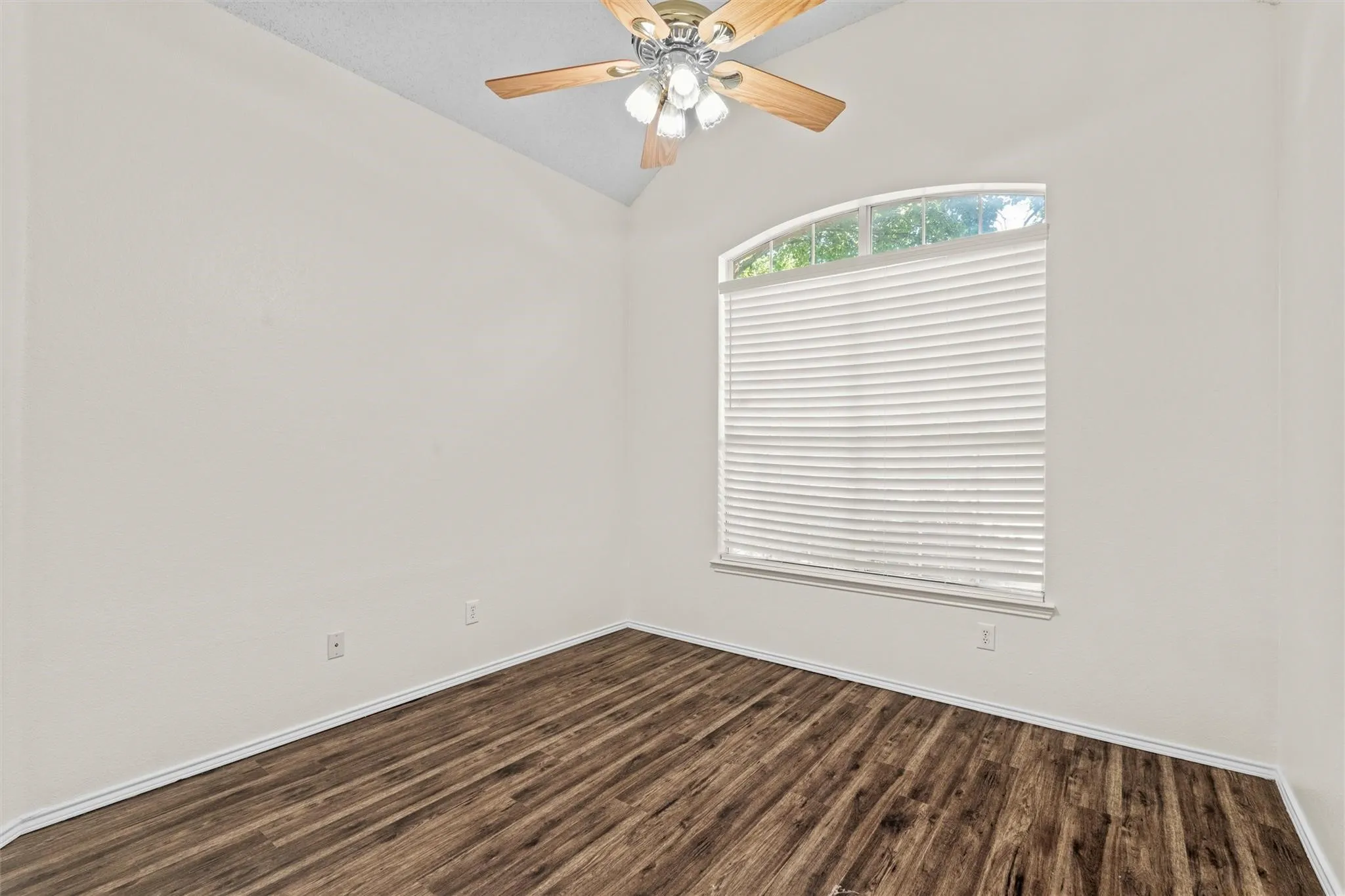 Vaulted ceiling with a ceiling fan, wood-finish flooring, and an arched window with blinds