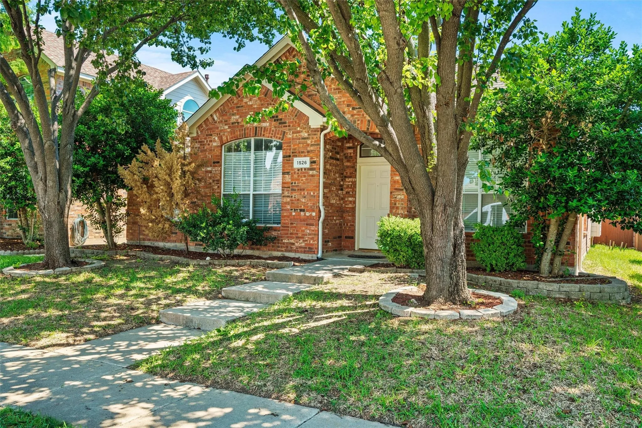 Red brick exterior with an arched window, white entry door, and a concrete pathway