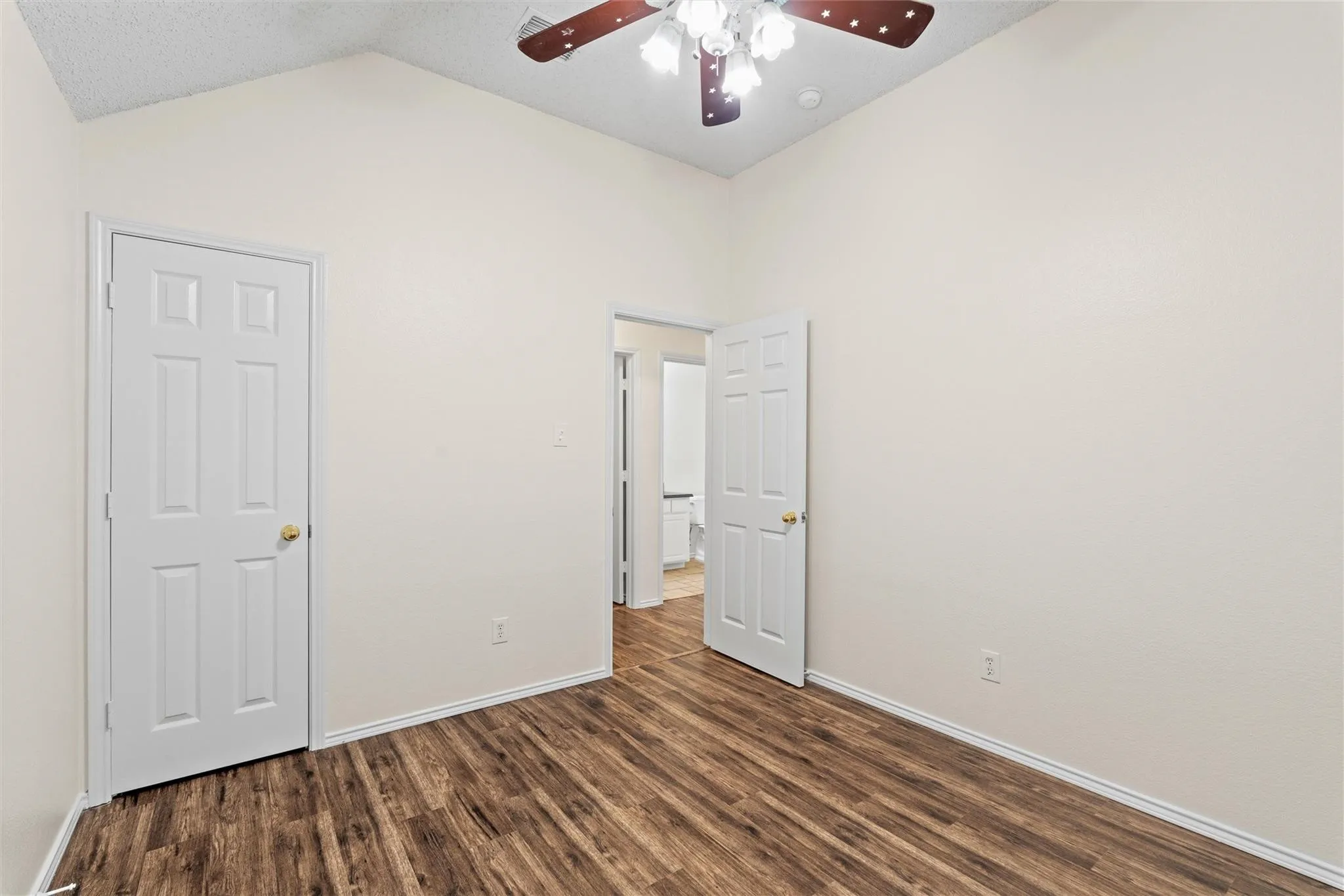 Vaulted ceiling with a ceiling fan, wood-finish flooring, and white interior doors