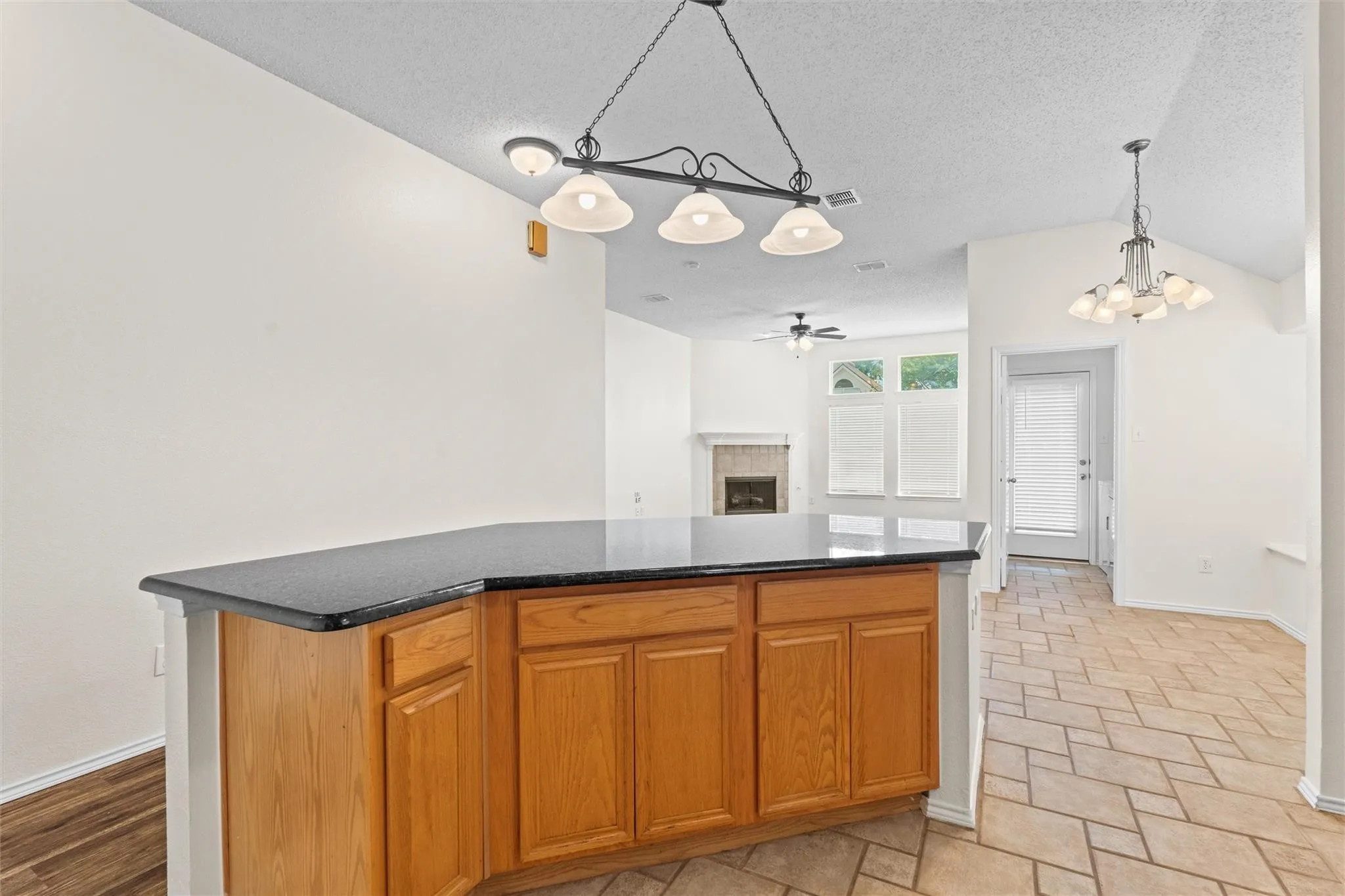Kitchen island with wood cabinetry, dark countertop, and overhead chandelier