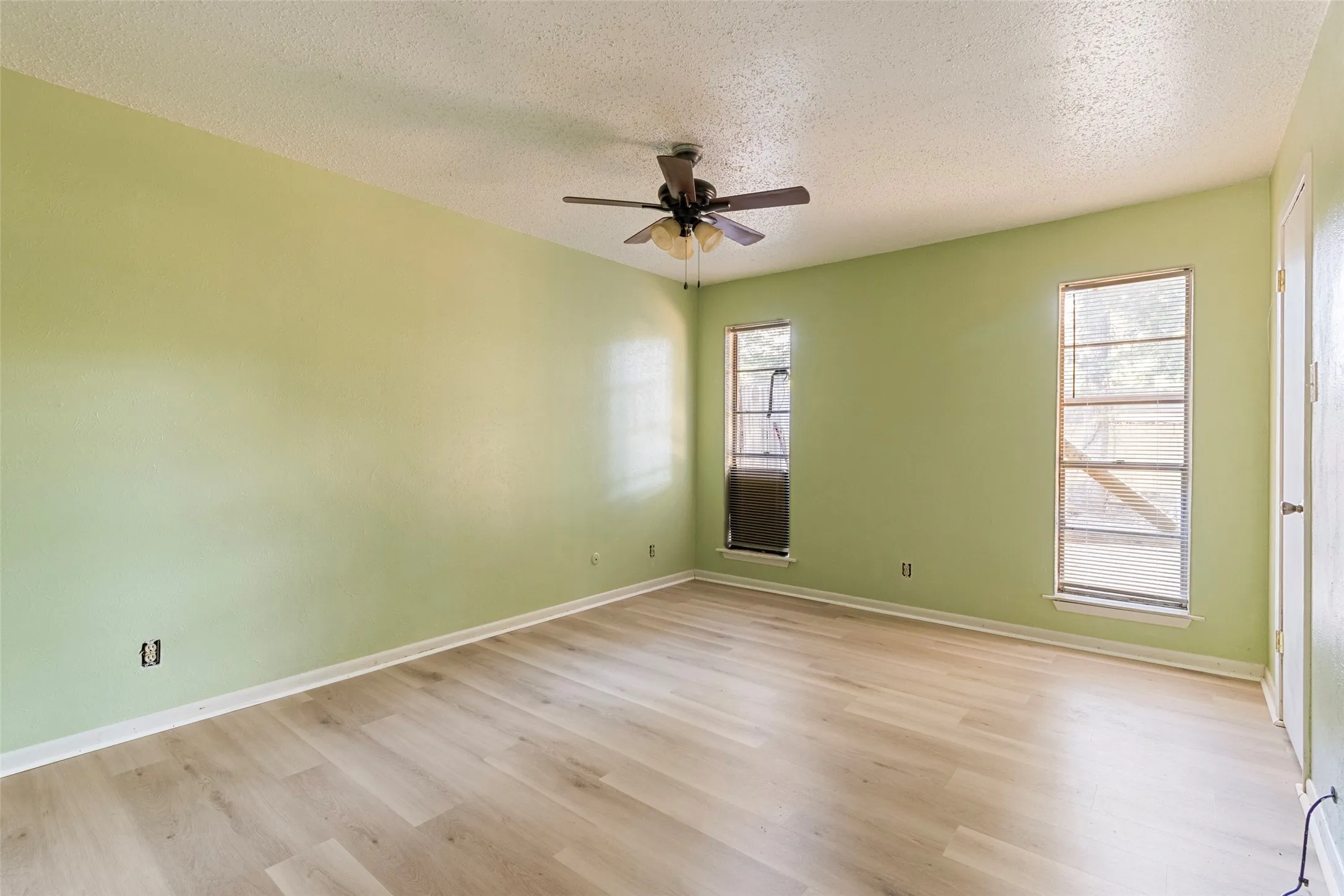 Room featuring wood-finish flooring, two windows, and a ceiling fan with integrated lighting