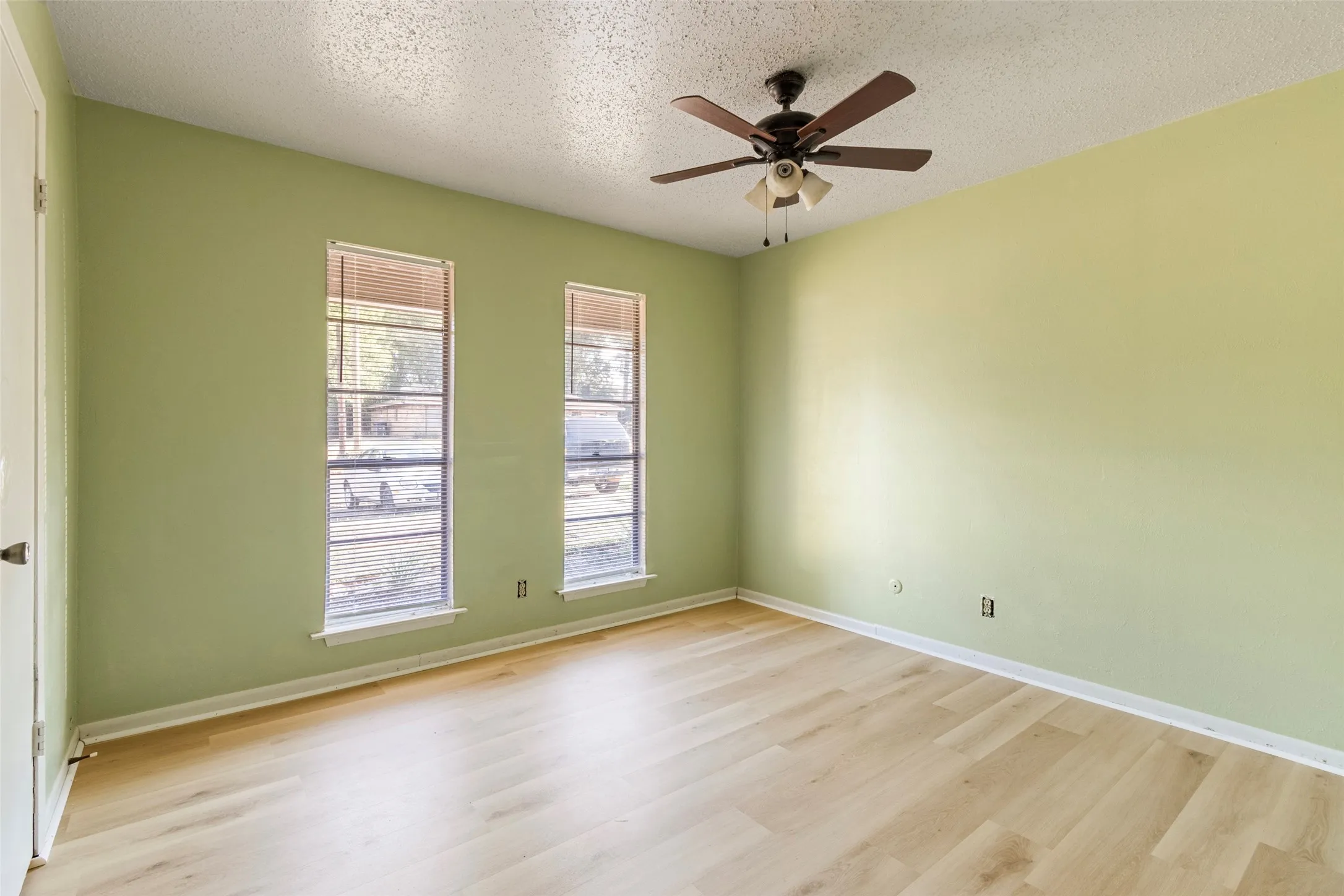 Wood-finish flooring, two large windows with blinds, and a ceiling fan with integrated lighting