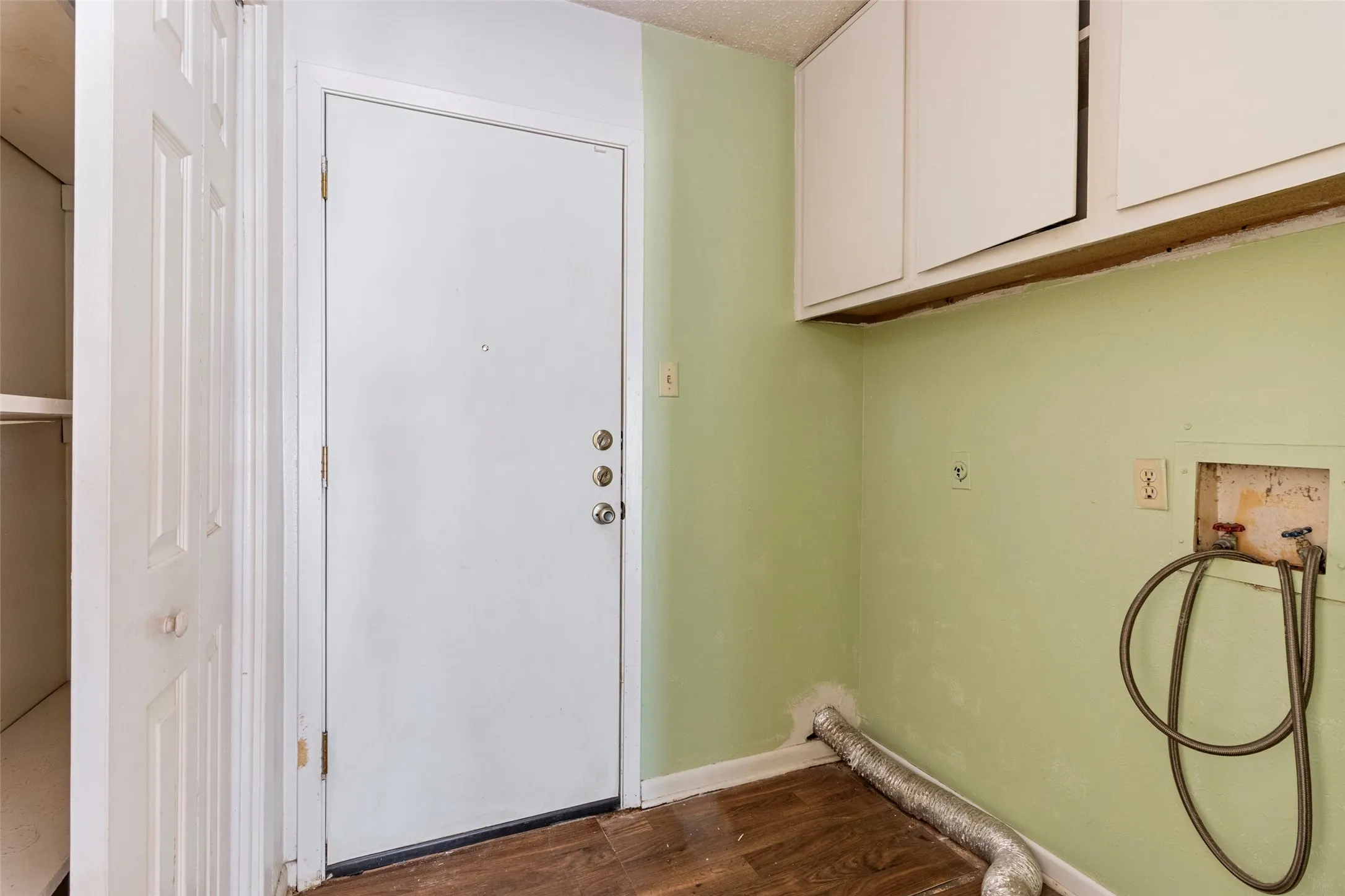 Utility area featuring wood-finish flooring, white cabinetry, and a bi-fold closet with shelving