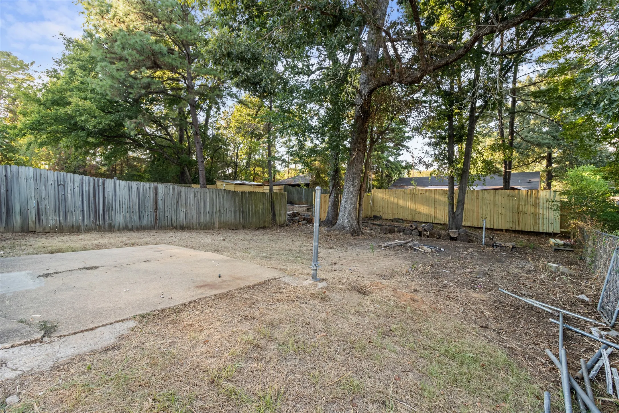 Expansive backyard with a concrete patio, mature trees, and privacy fencing