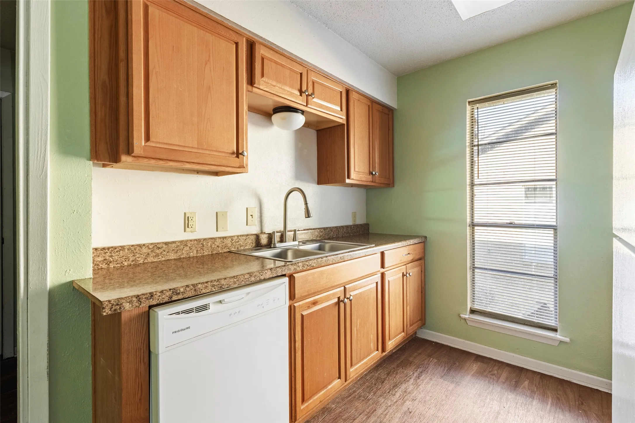 Kitchen with wood-finish cabinetry, a double basin sink with a high-arc faucet, and granite-look countertops