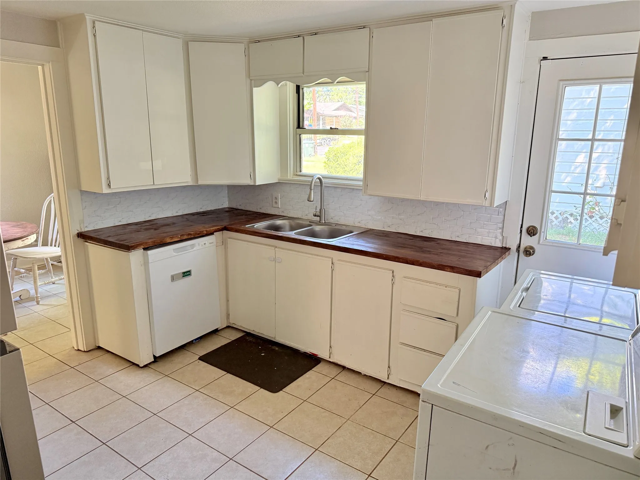 White cabinetry, wood-finish countertops, tile backsplash, built-in dishwasher, and tile flooring