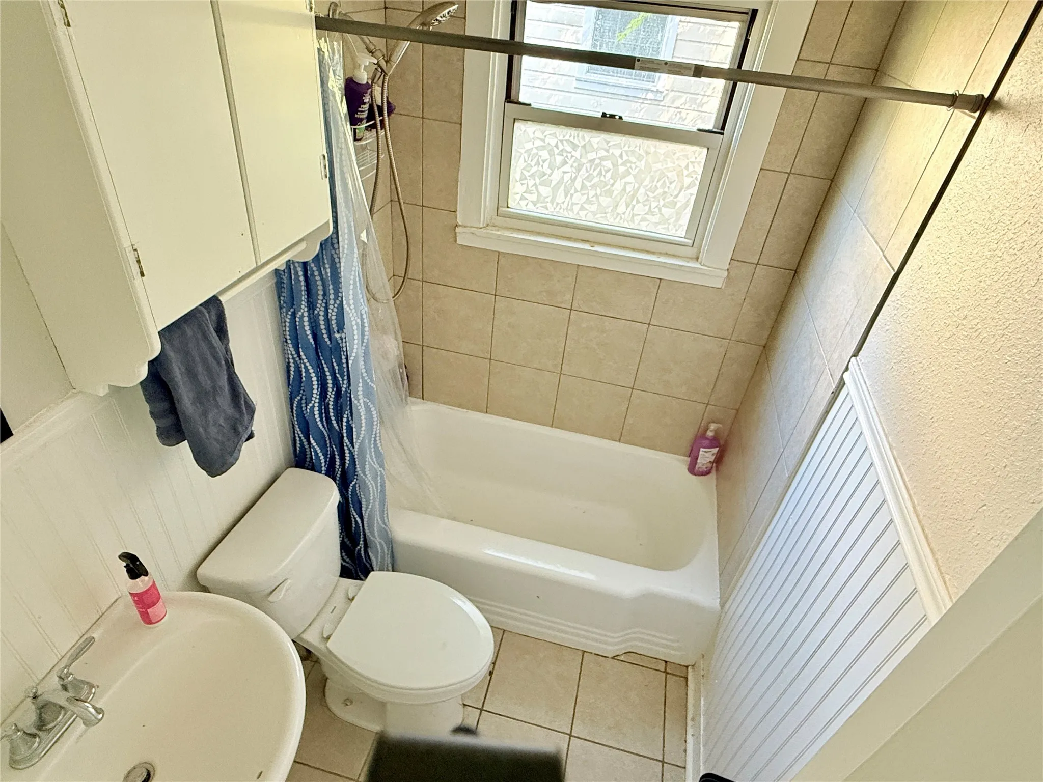 Built-in white cabinetry, shower/tub combination, tiled walls, and beadboard paneling