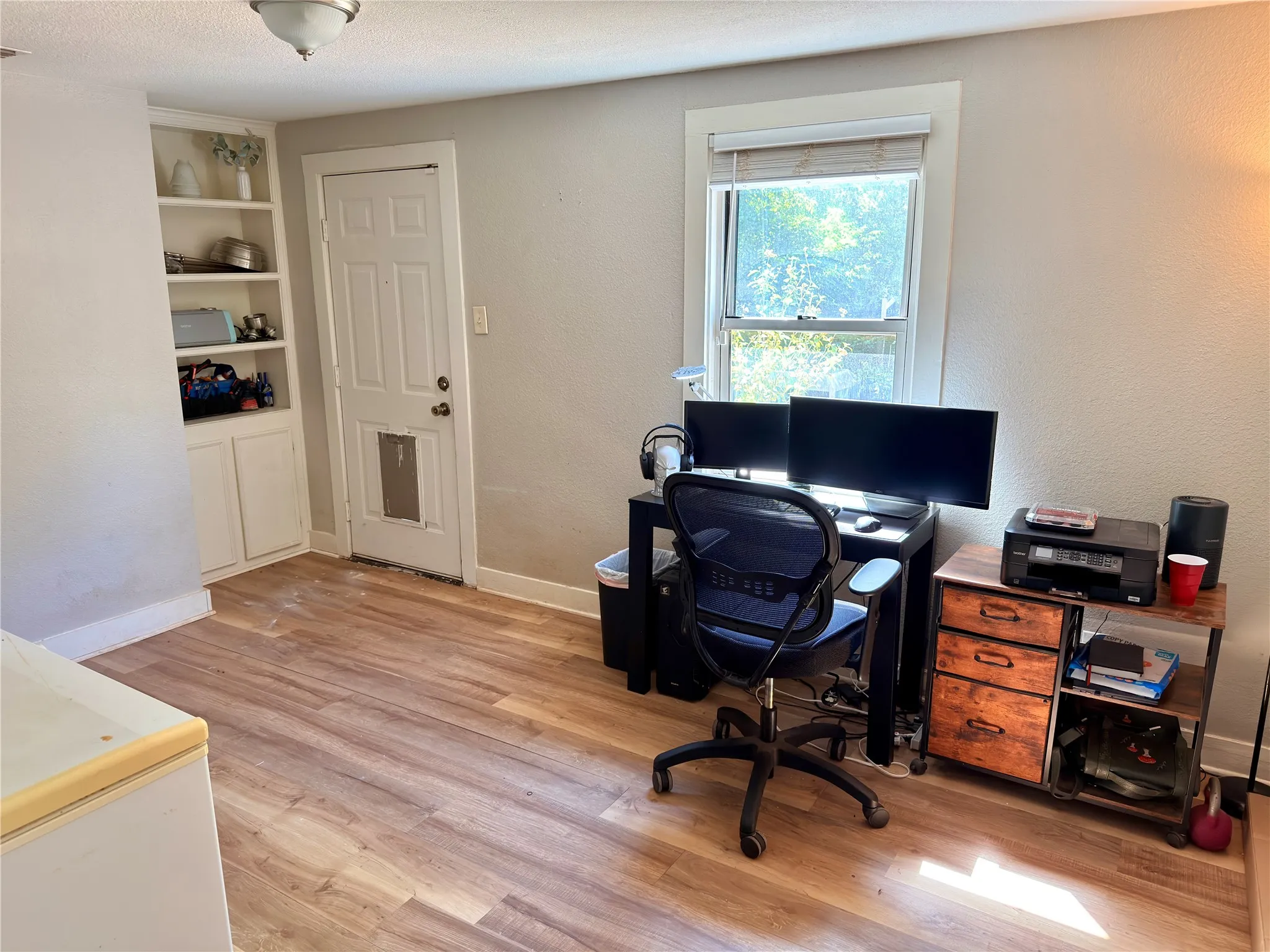 Wood-finish flooring, built-in shelving with lower cabinetry, and a window with blinds