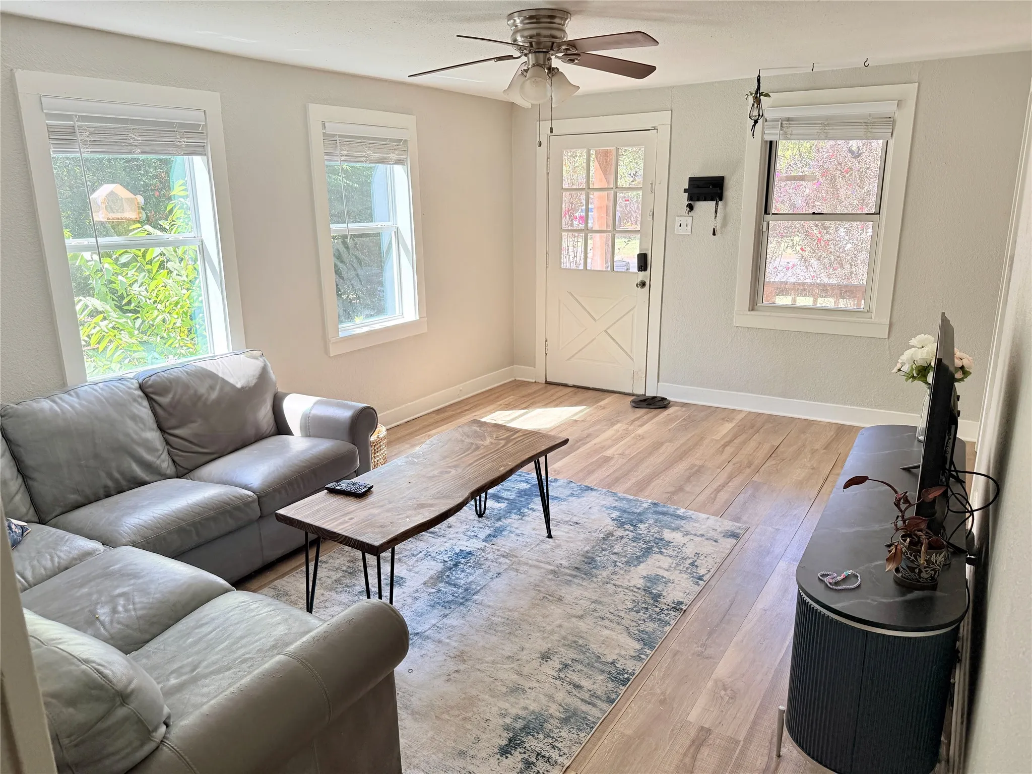 Wood-finish flooring, white trim, multiple windows, ceiling fan with light fixture, and a white door with glass panels