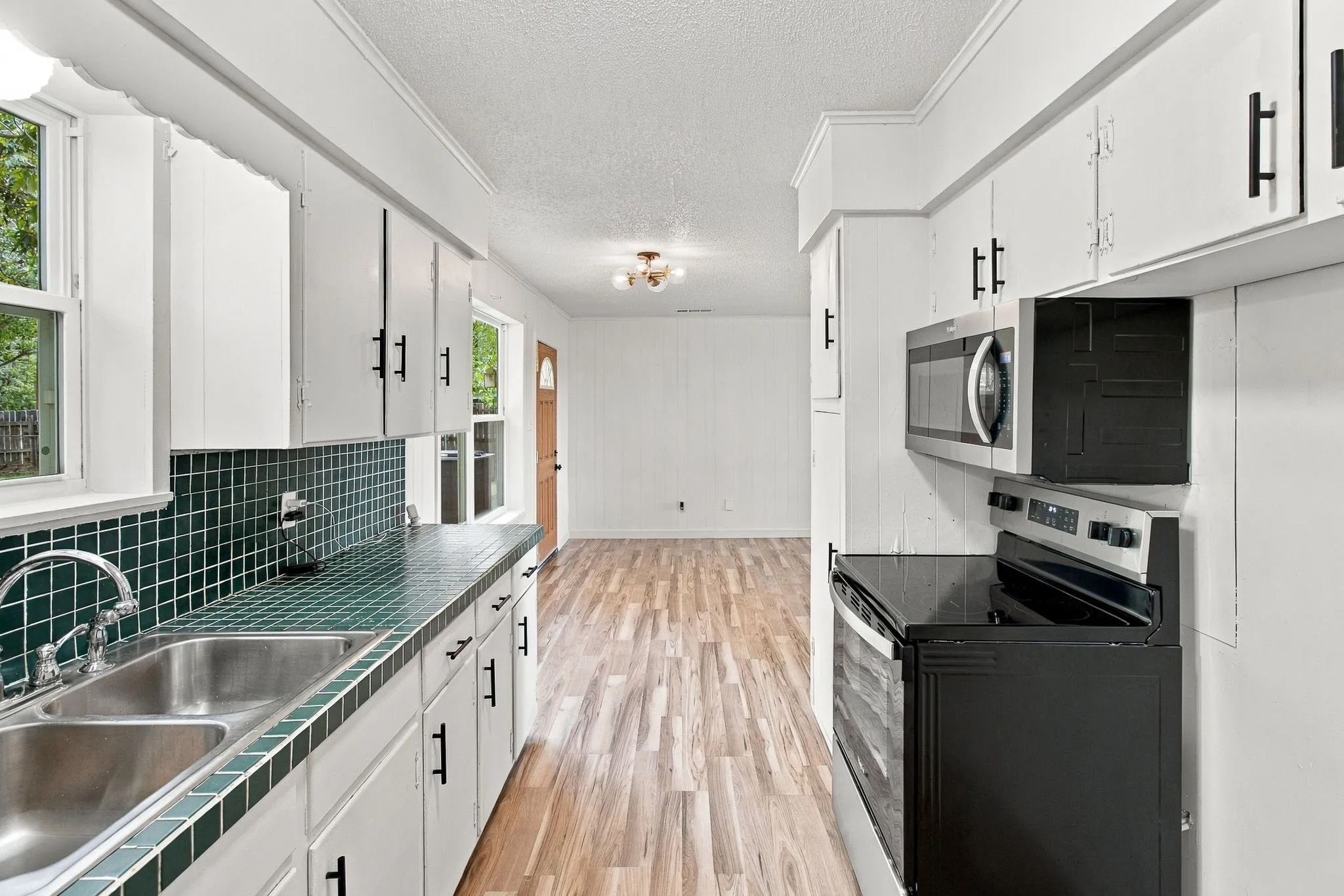 Galley kitchen featuring white cabinetry, dark tile countertops, a double basin stainless steel sink, and wood-finish flooring