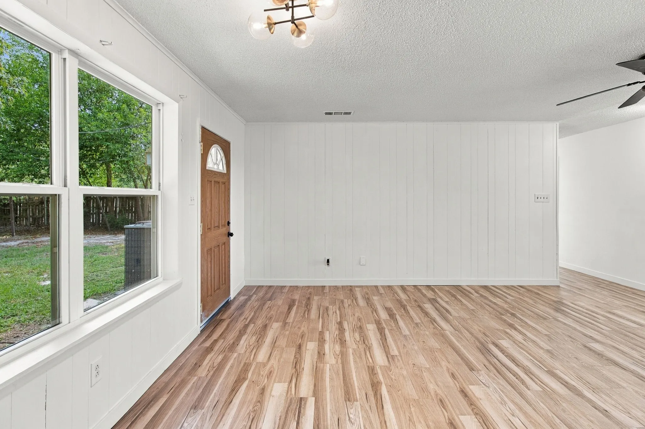 LVP flooring throughout, white paneled wall accents, white trimmed windows, a brown entry door with an arched glass insert, and an updated ceiling light fixture