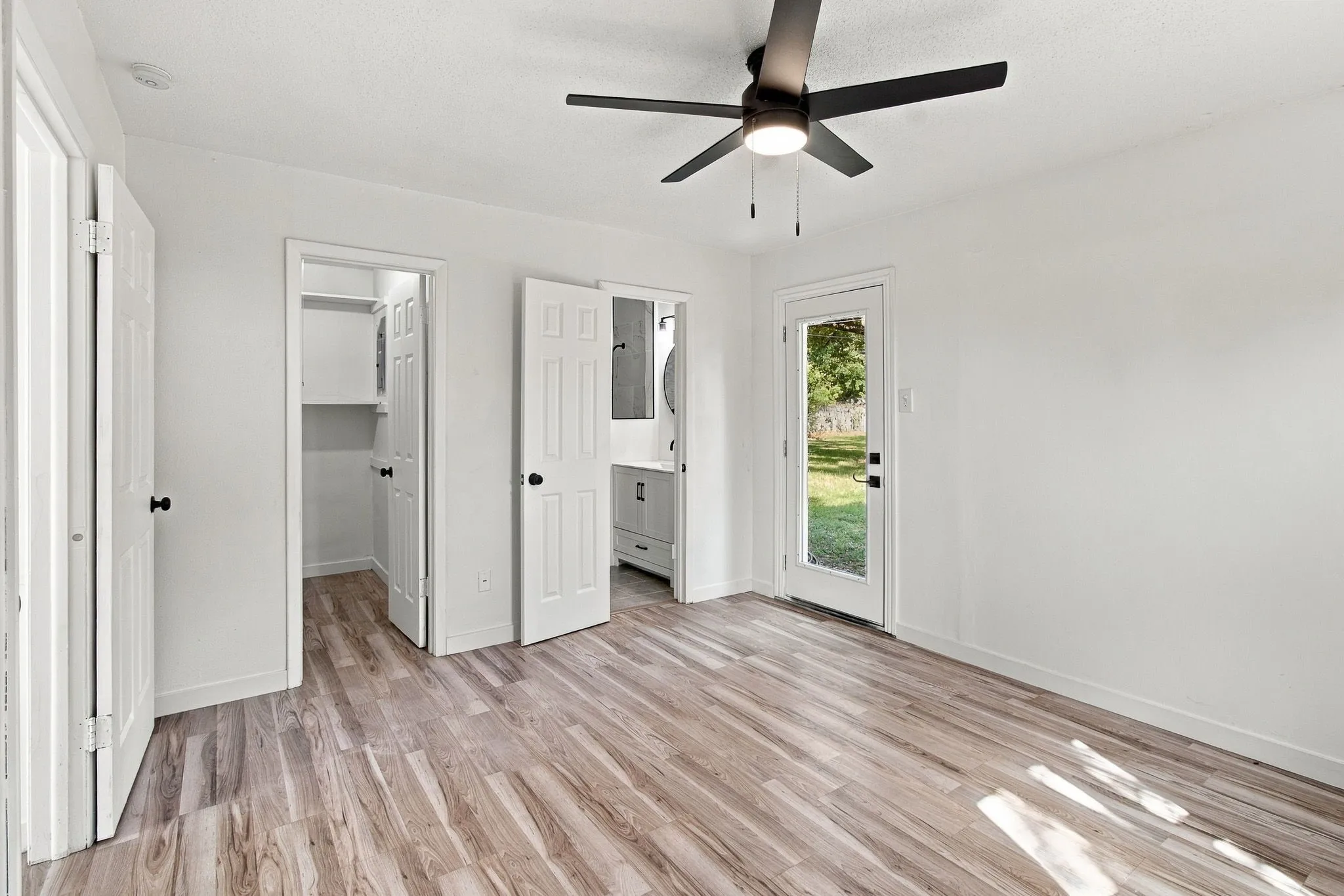 LVP flooring, white walls, black ceiling fan with integrated lighting, built-in closet shelving, and a glass-paneled exterior door