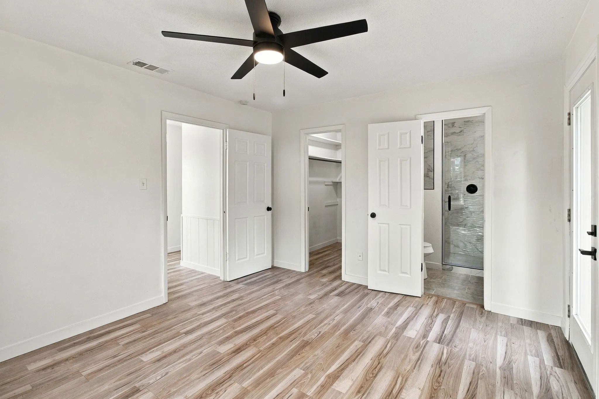 LVP flooring, white walls, black ceiling fan, white paneled doors, and a walk-in closet