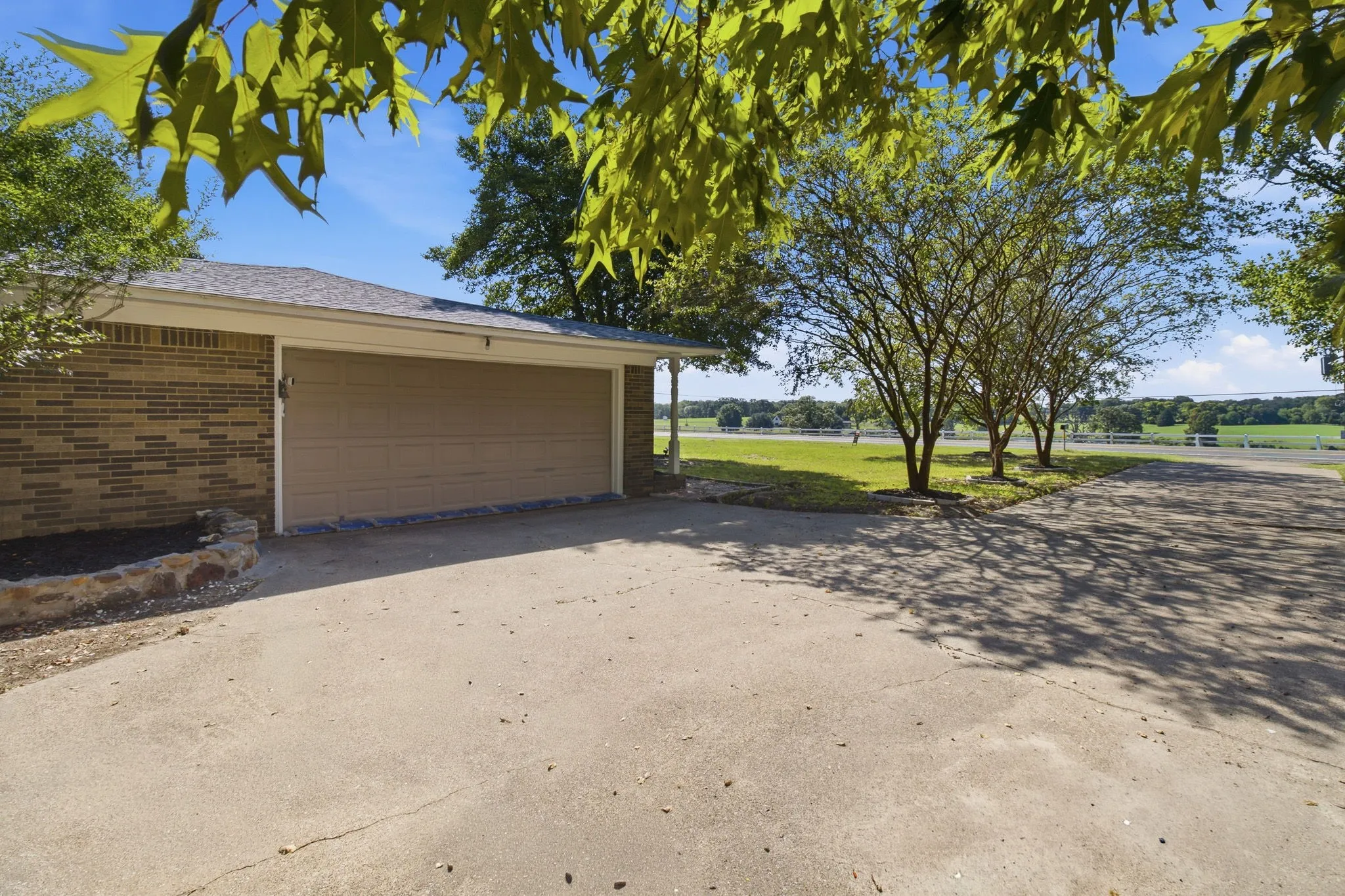 Attached two-car garage with a concrete driveway, brick exterior, and landscaped beds