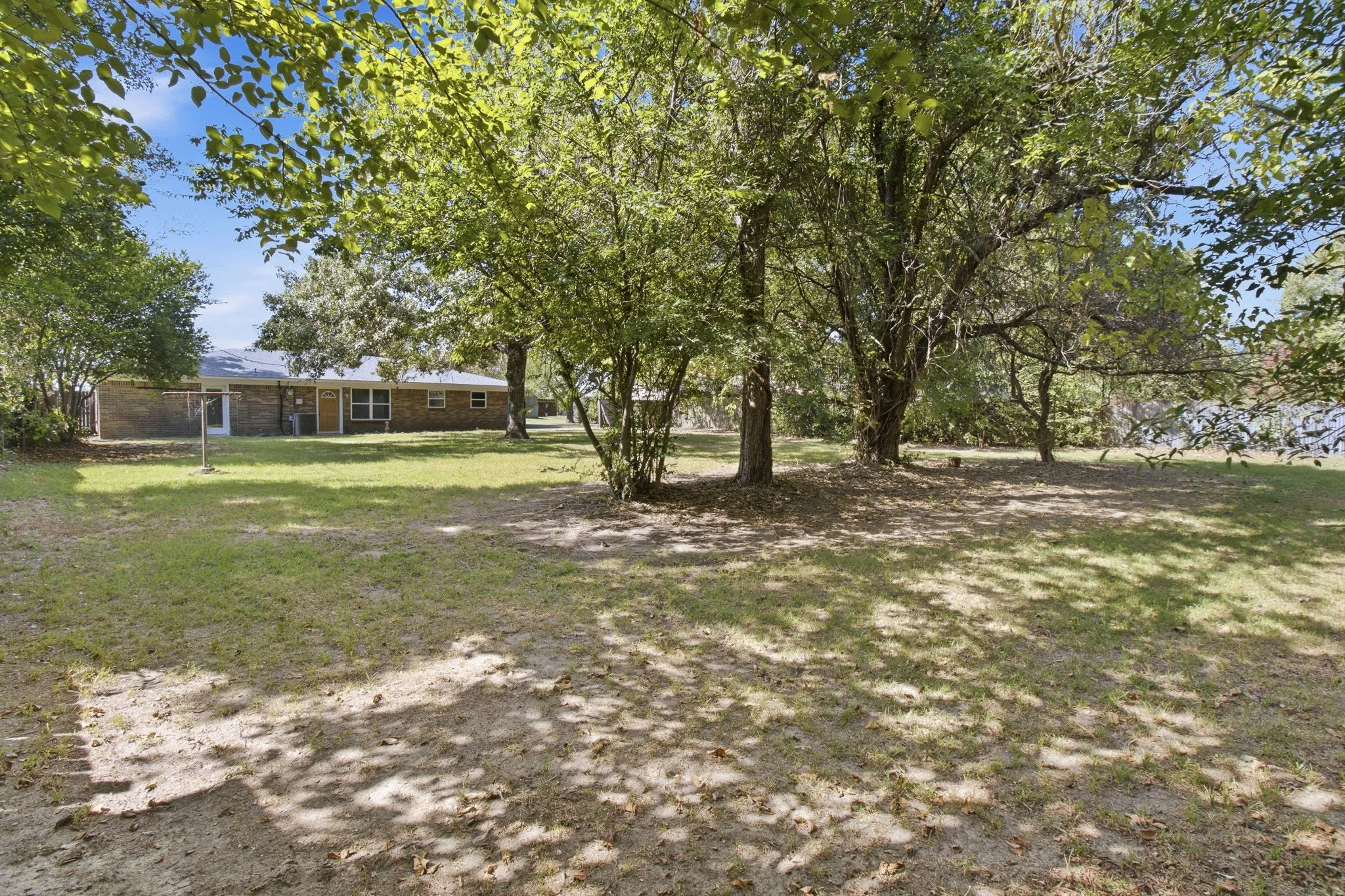 Expansive backyard featuring mature trees, a manicured lawn, and brick exterior