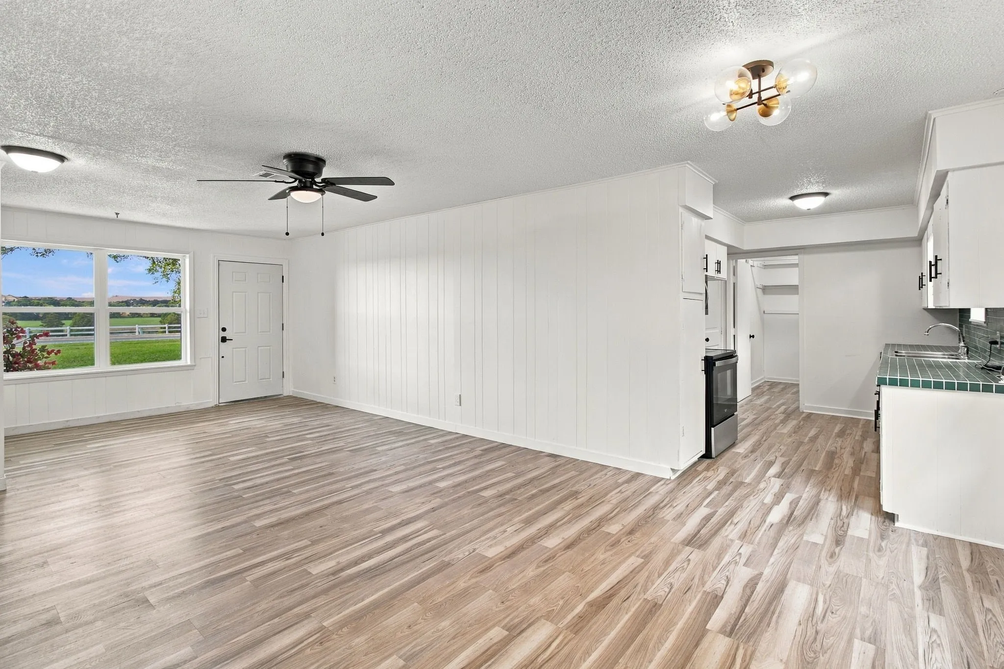LVP flooring throughout, white walls, modern ceiling fan, contemporary ceiling light fixture, and white cabinetry with dark hardware