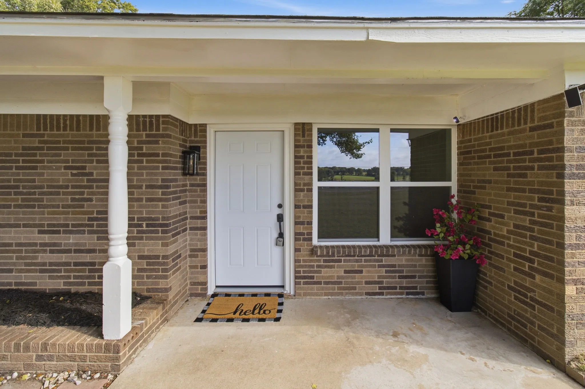 Brick exterior with a covered entry, decorative column, white paneled door, and multi-pane window