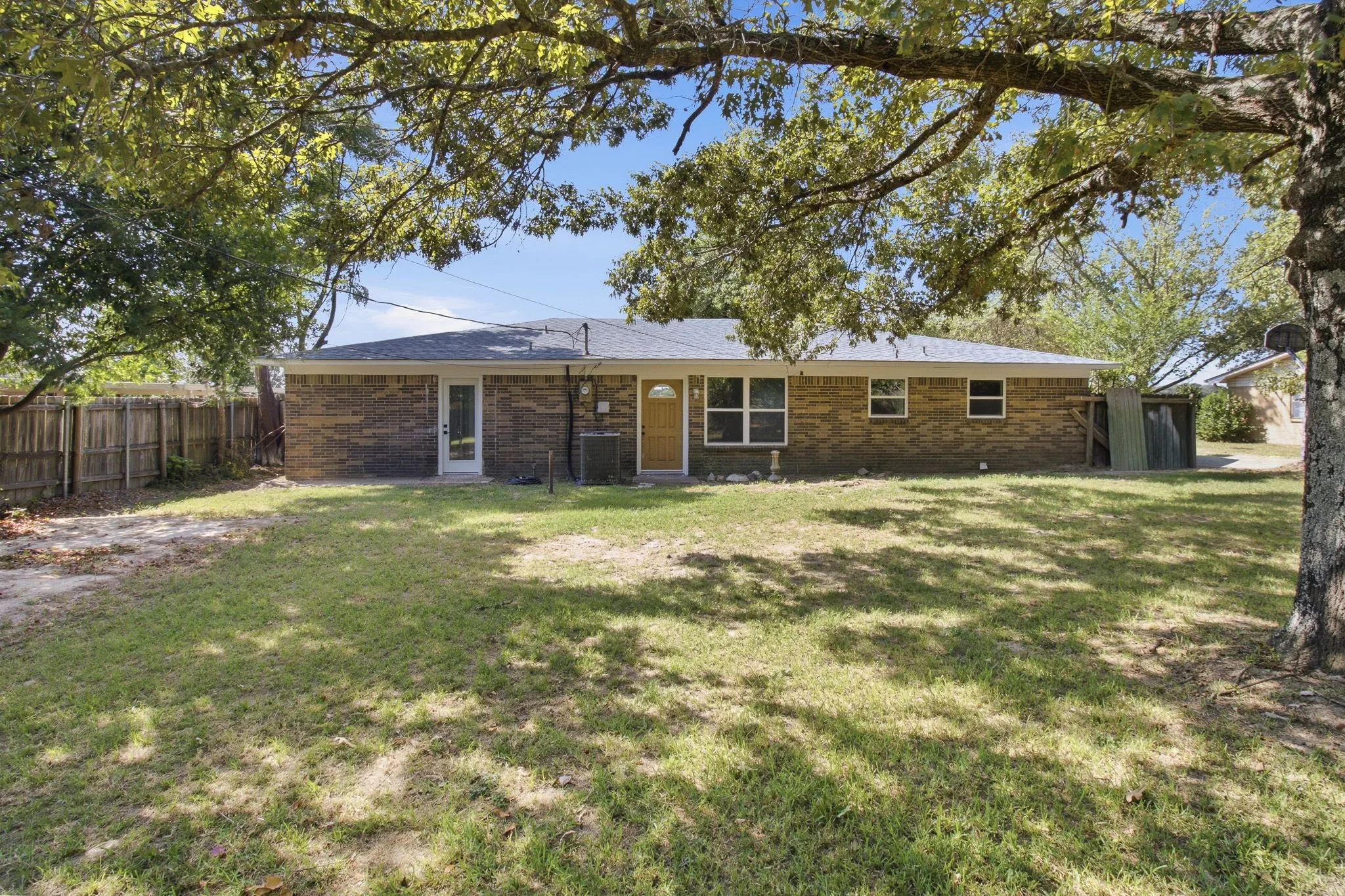Brick exterior with multiple windows, a rear door with full-length glass, and mature trees providing natural shading
