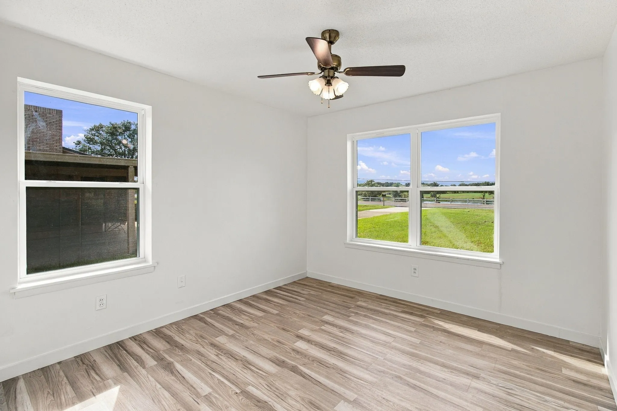 White walls, LVP flooring, two large windows, and a ceiling fan with integrated lighting