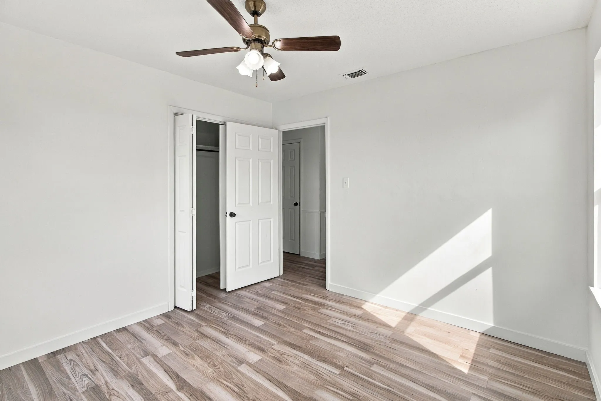 LVP  flooring, ceiling fan with light fixture, white interior paint, bi-fold closet doors, and recessed window