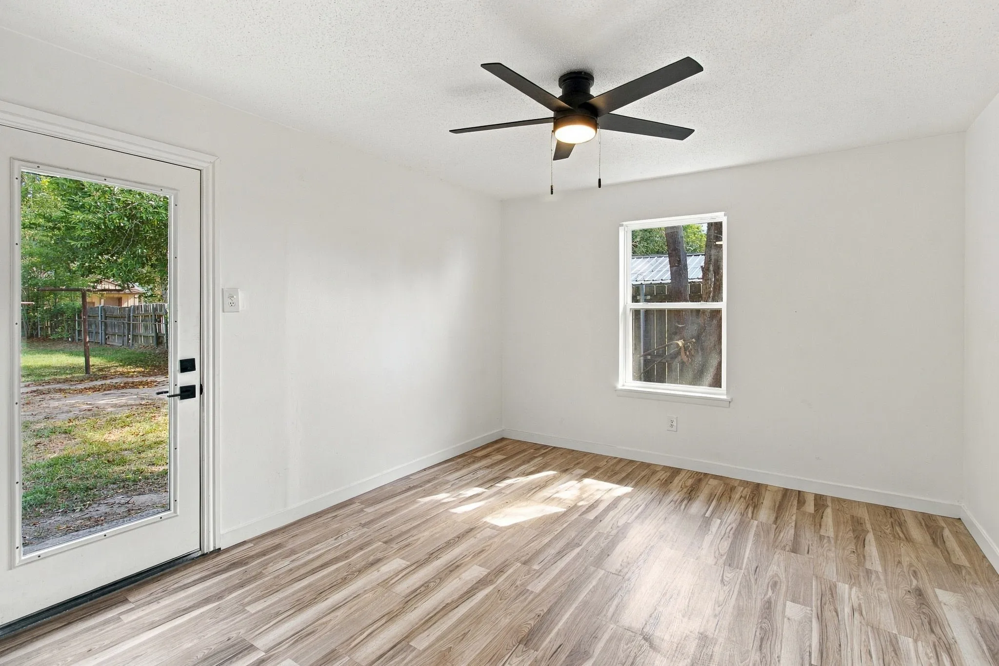 Crisp white walls, LVP flooring, black ceiling fan with integrated lighting, and a glass-paneled exterior door