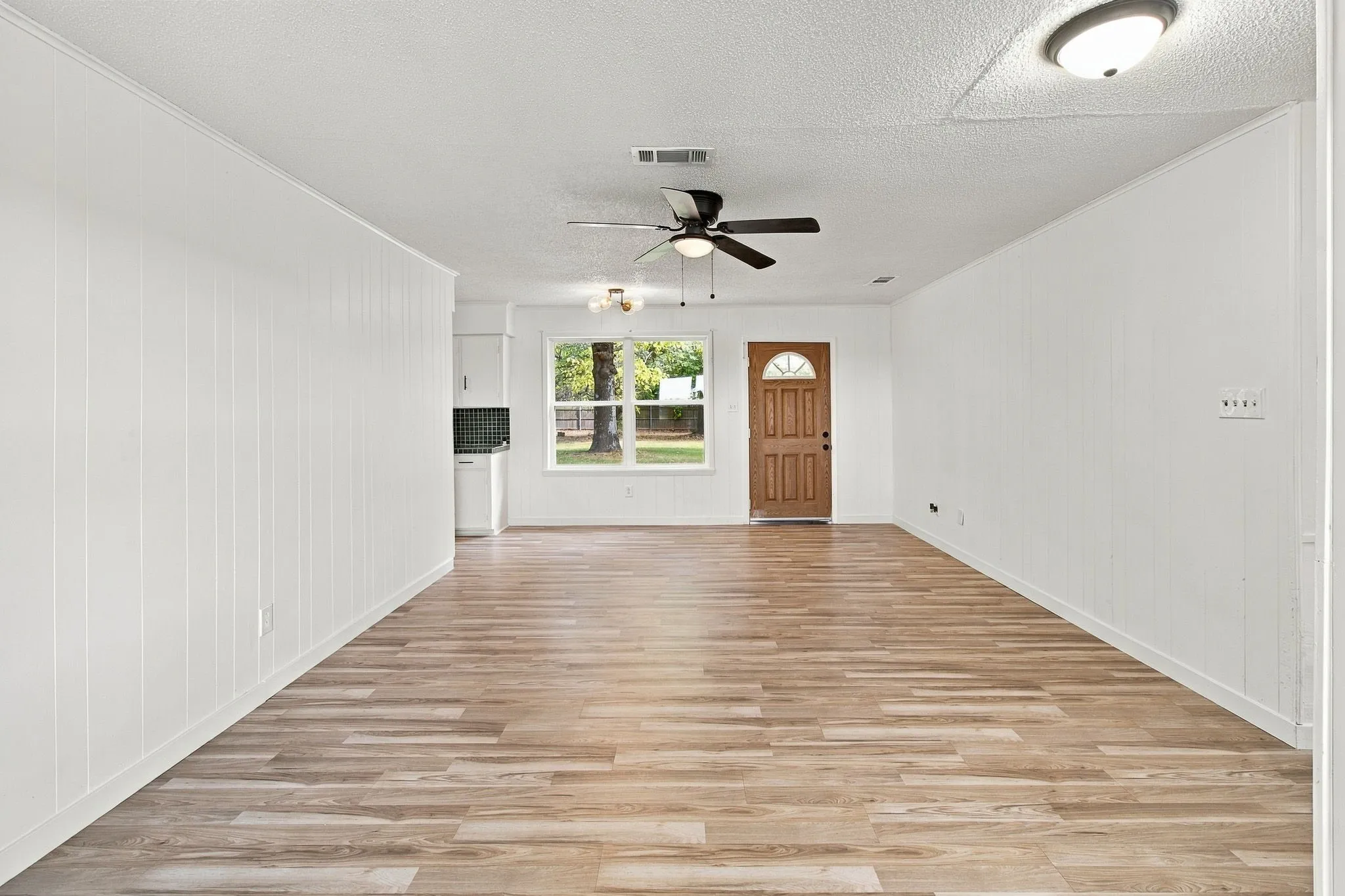 LVP flooring, white panel walls, ceiling fan, natural light from a front window, and a paneled front entry door
