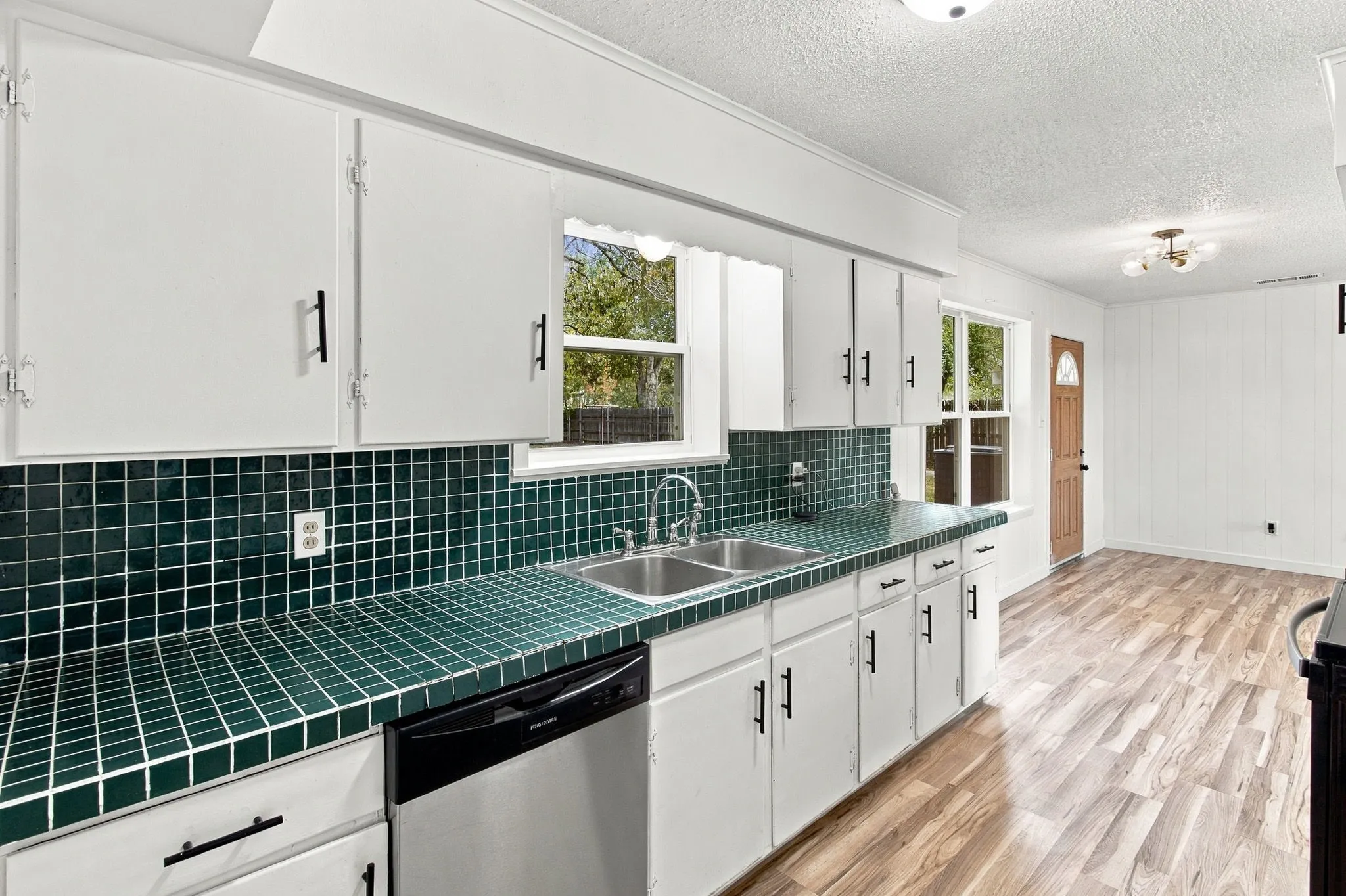 White cabinetry, green tiled countertops, stainless steel double basin sink, dishwasher, and wood-finish flooring