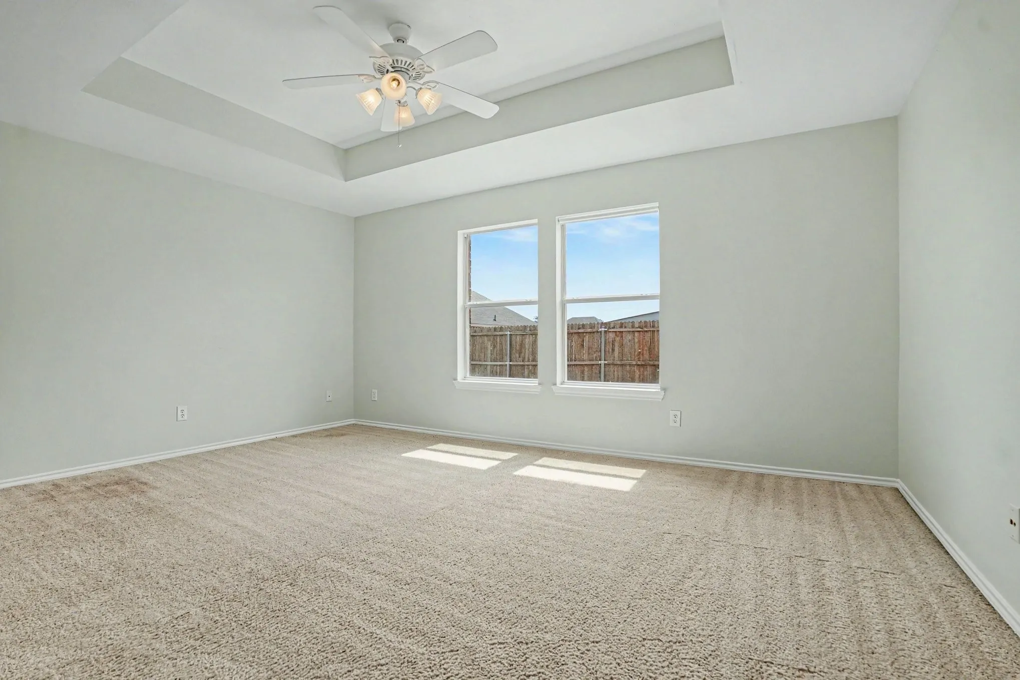 Tray ceiling with a ceiling fan light fixture, two windows, and neutral carpeting