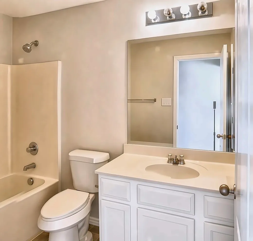 Bathroom 2, featuring a white vanity with a single basin sink, integrated countertop, and a vanity mirror with overhead lighting