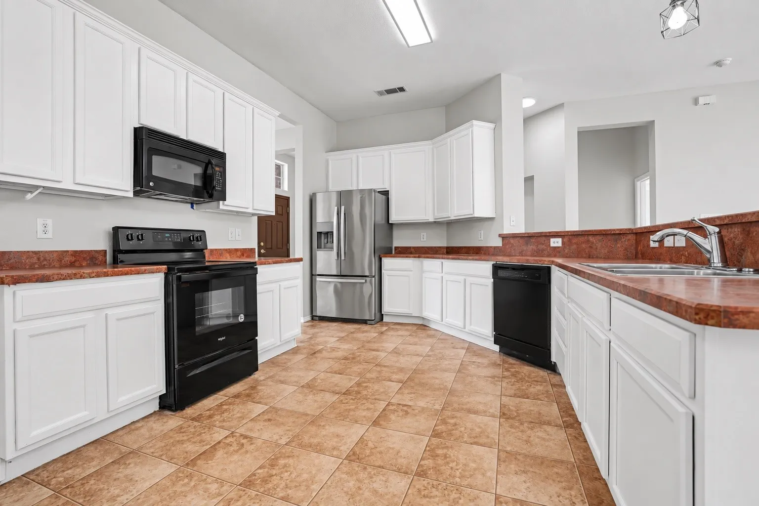 Kitchen featuring white cabinetry, a stainless steel refrigerator, black range and microwave, and a double basin sink with a chrome faucet