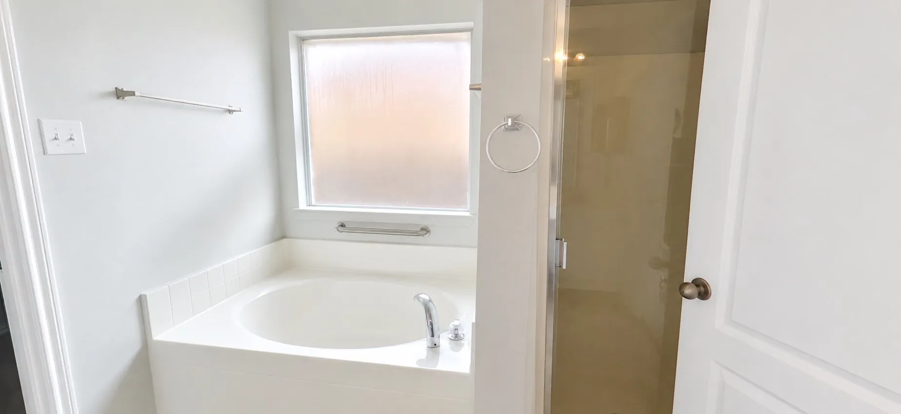 Built-in soaking tub with chrome fixtures, frosted window, and glass-enclosed shower