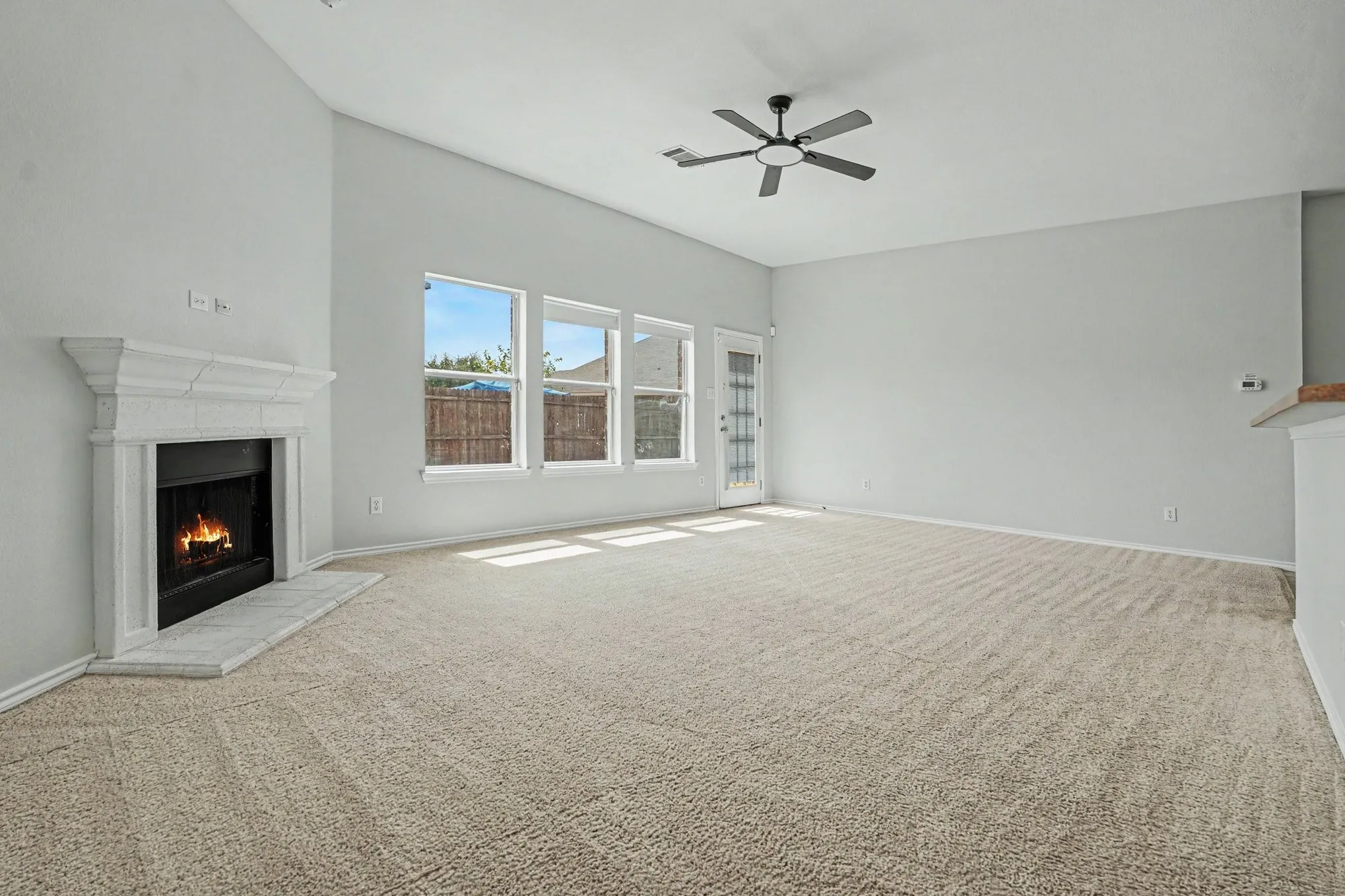 Fireplace with decorative mantle, multiple windows, built-in ceiling fan, light-colored carpeting, and a glass-paneled door