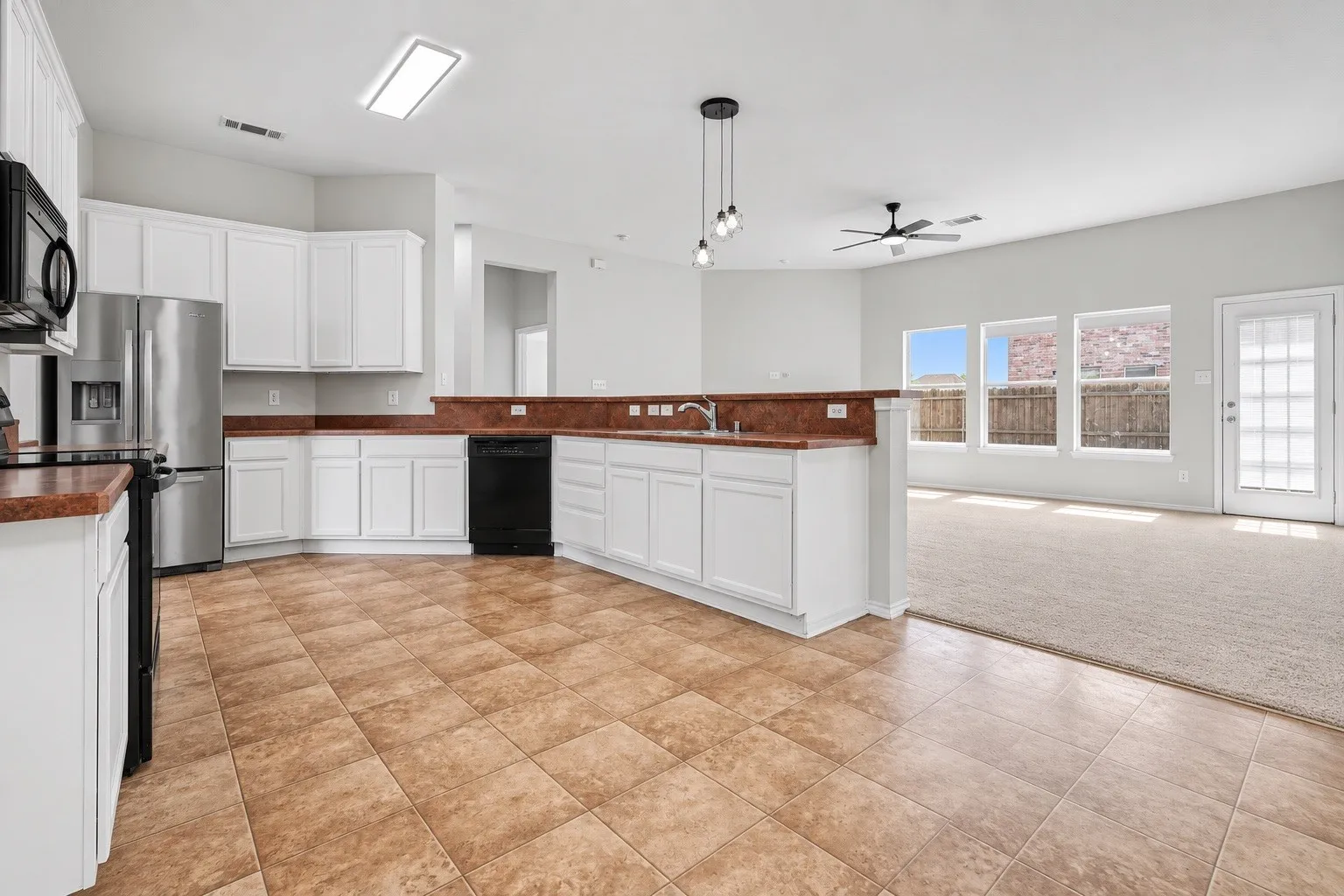 Kitchen featuring white cabinetry, integrated stainless steel appliances, tile flooring, and a breakfast bar overlooking a carpeted living area with multiple windows