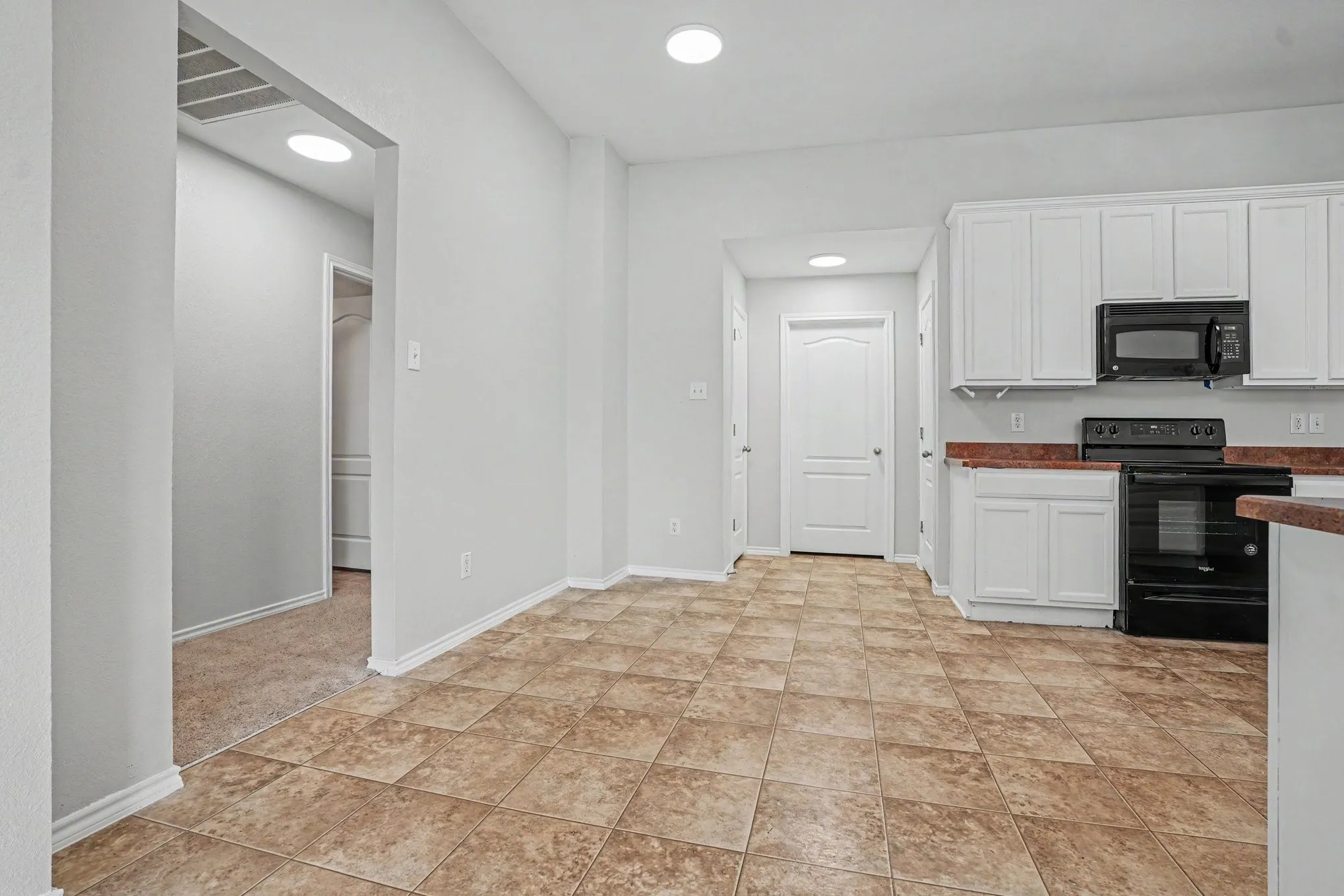 Kitchen featuring white cabinetry, black appliances, solid surface countertops, and tile flooring