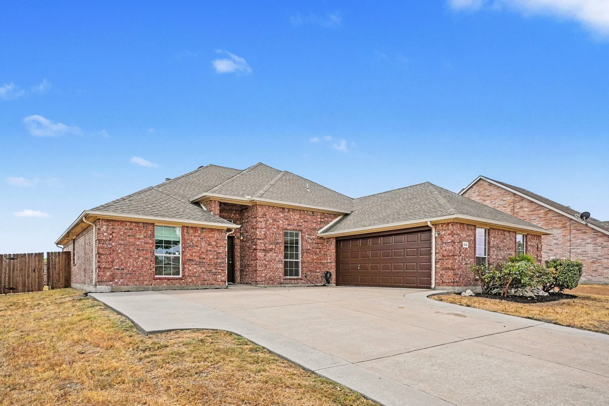 Brick exterior with an attached two-car garage, concrete driveway, and partial wood fencing