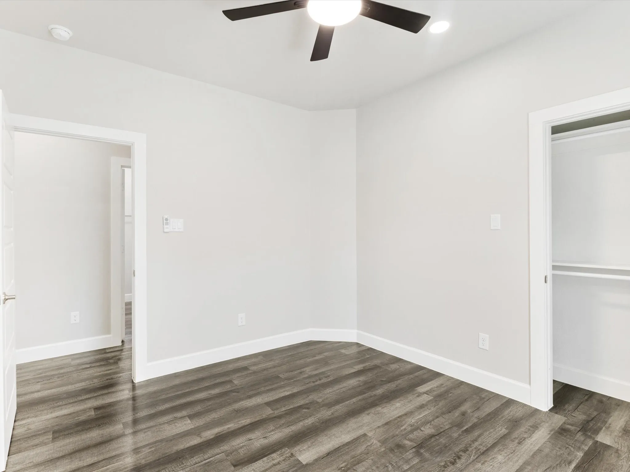 Room featuring wood-finish flooring, white walls, a ceiling fan with integrated lighting, and a closet with shelving