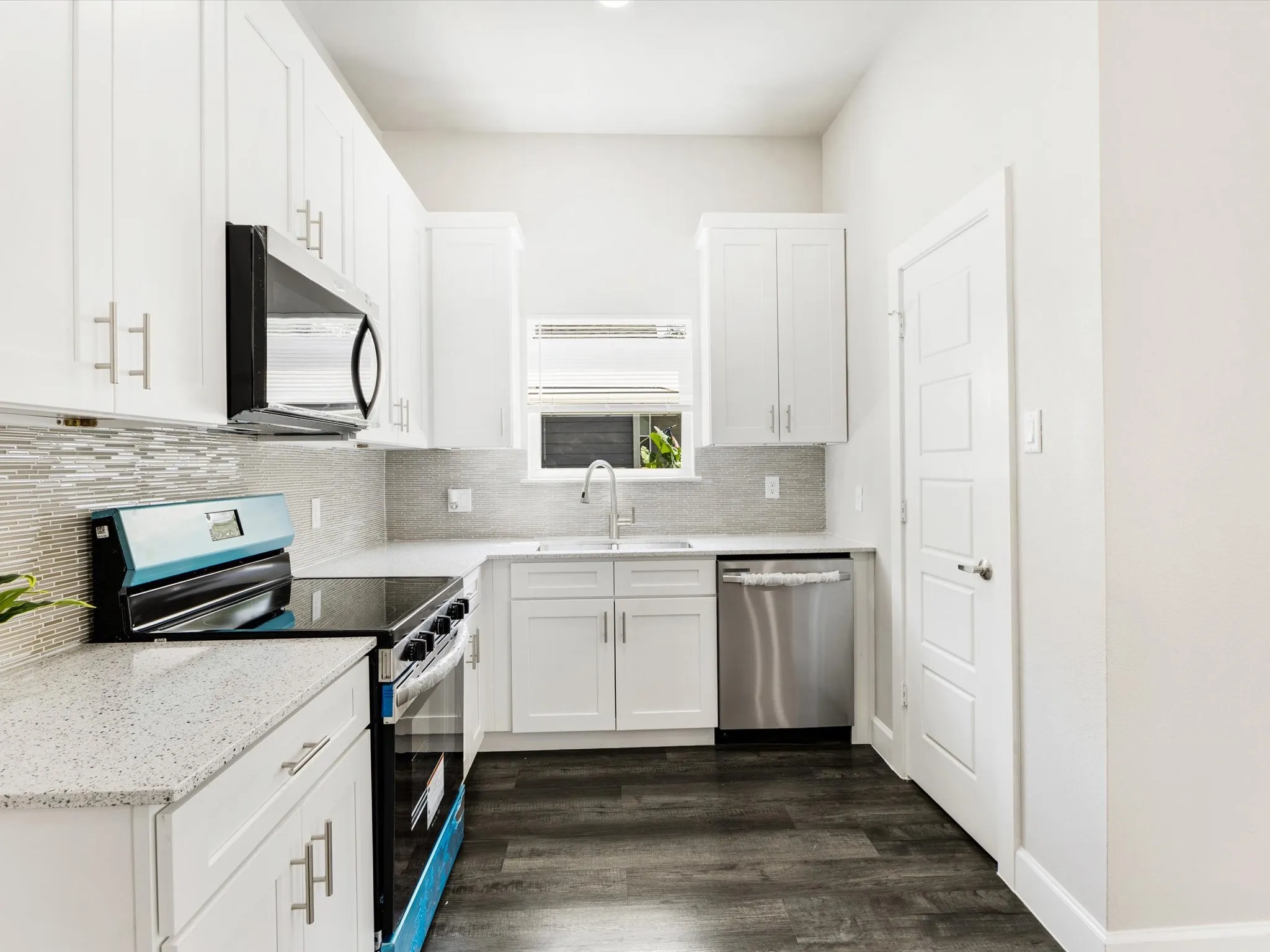 Kitchen featuring white shaker cabinetry, speckled countertops, stainless steel appliances, a tile backsplash, and wood-finish flooring
