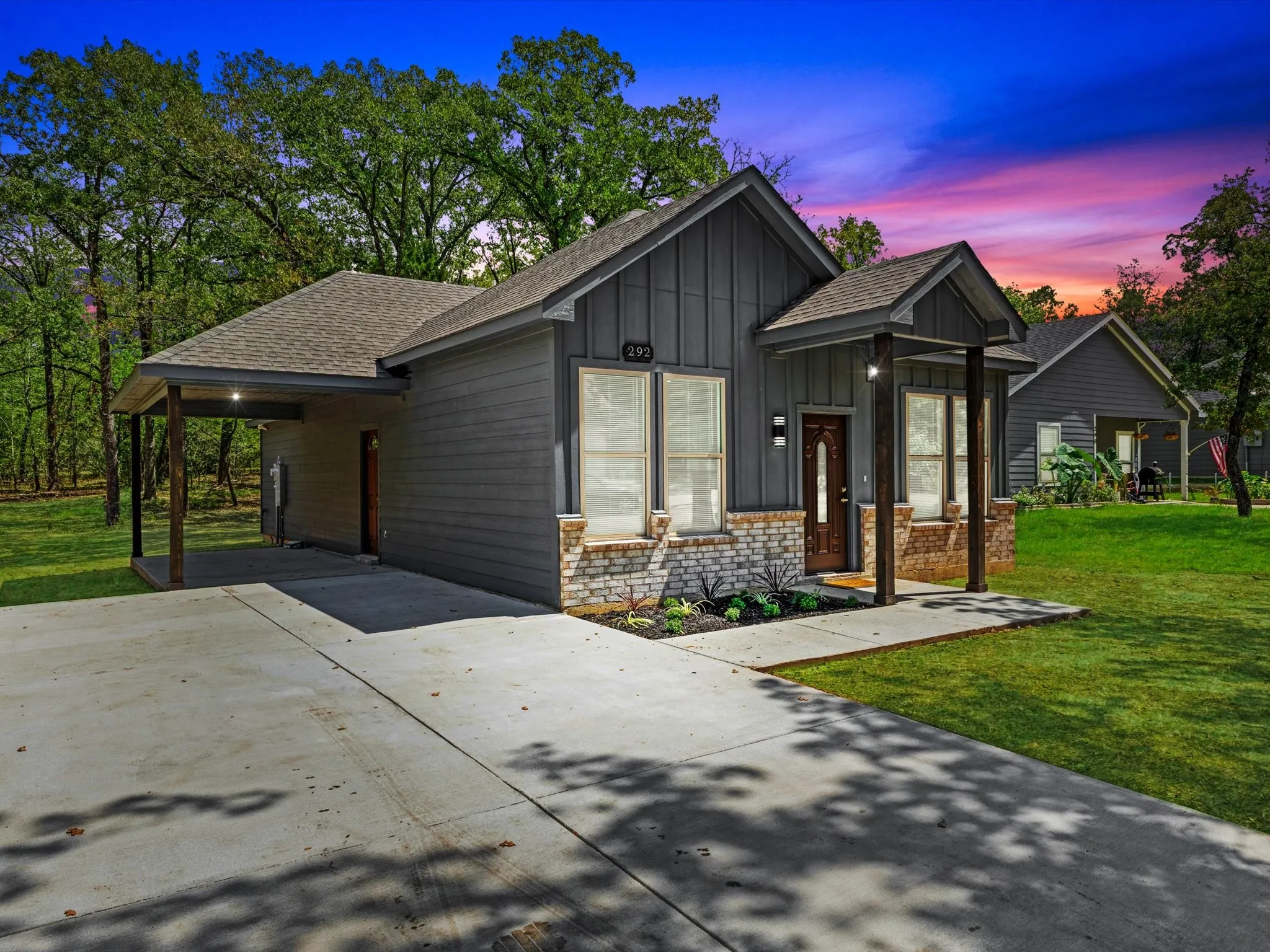 Contemporary exterior featuring board and batten siding, stone accents, a covered front entry, a single-car porte-cochère, and a concrete driveway