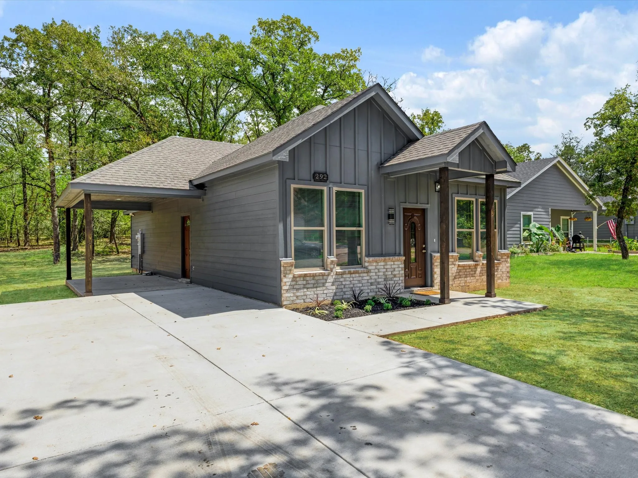 Contemporary exterior featuring a covered porch, board and batten siding, stone accents, a wood-finish front door, and an expansive concrete driveway