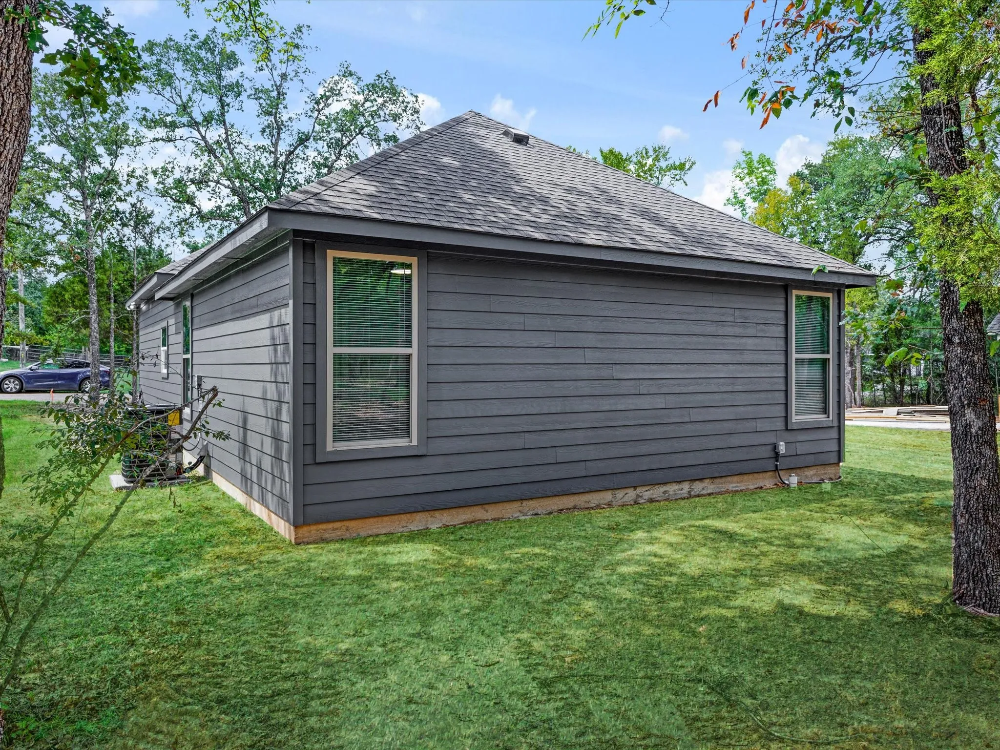 Exterior with gray horizontal siding, a dark shingle roof, and multiple windows with light-colored frames