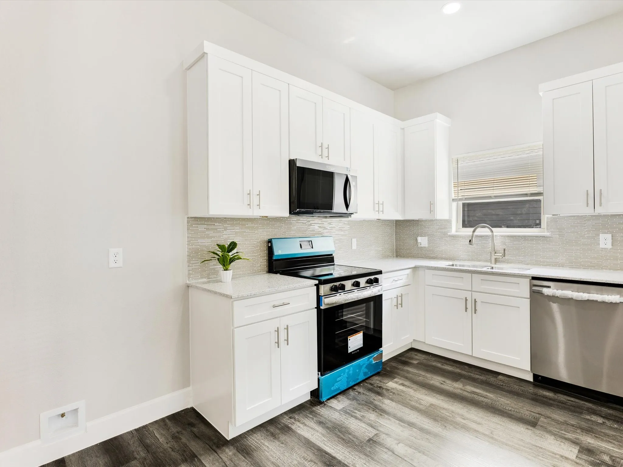 Modern kitchen featuring white cabinetry, stone countertops, stainless steel appliances, wood-finish flooring, and a tiled backsplash
