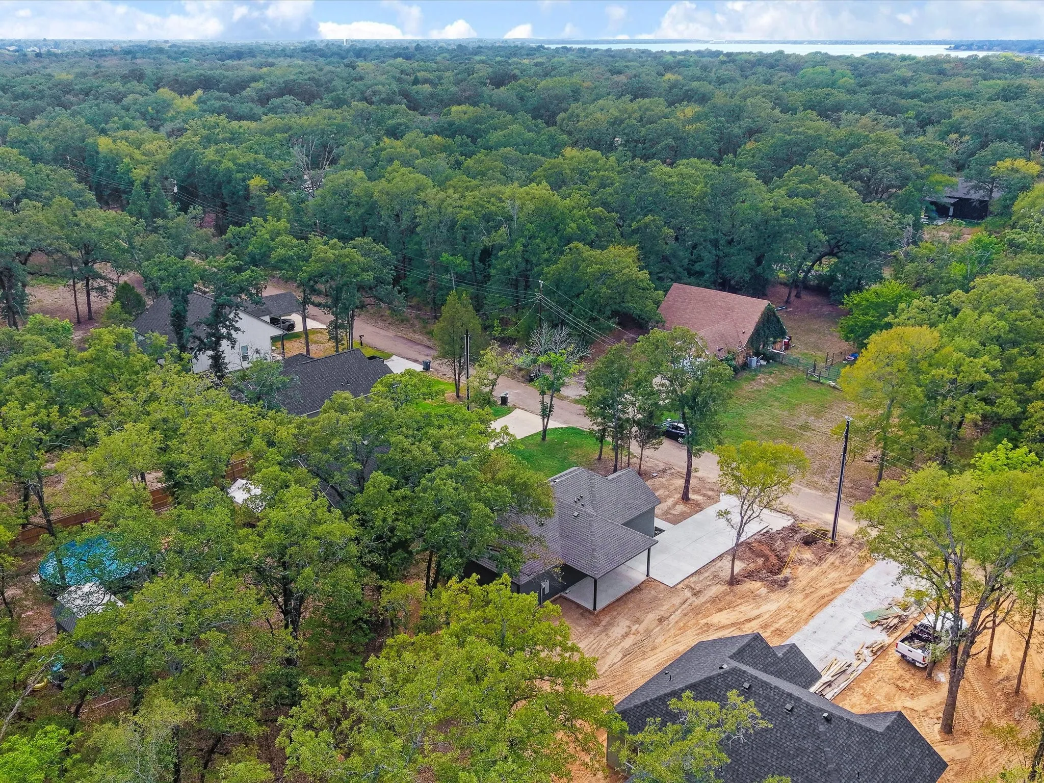 Expansive wooded surroundings with a new construction property featuring a dark shingle roof and concrete driveway