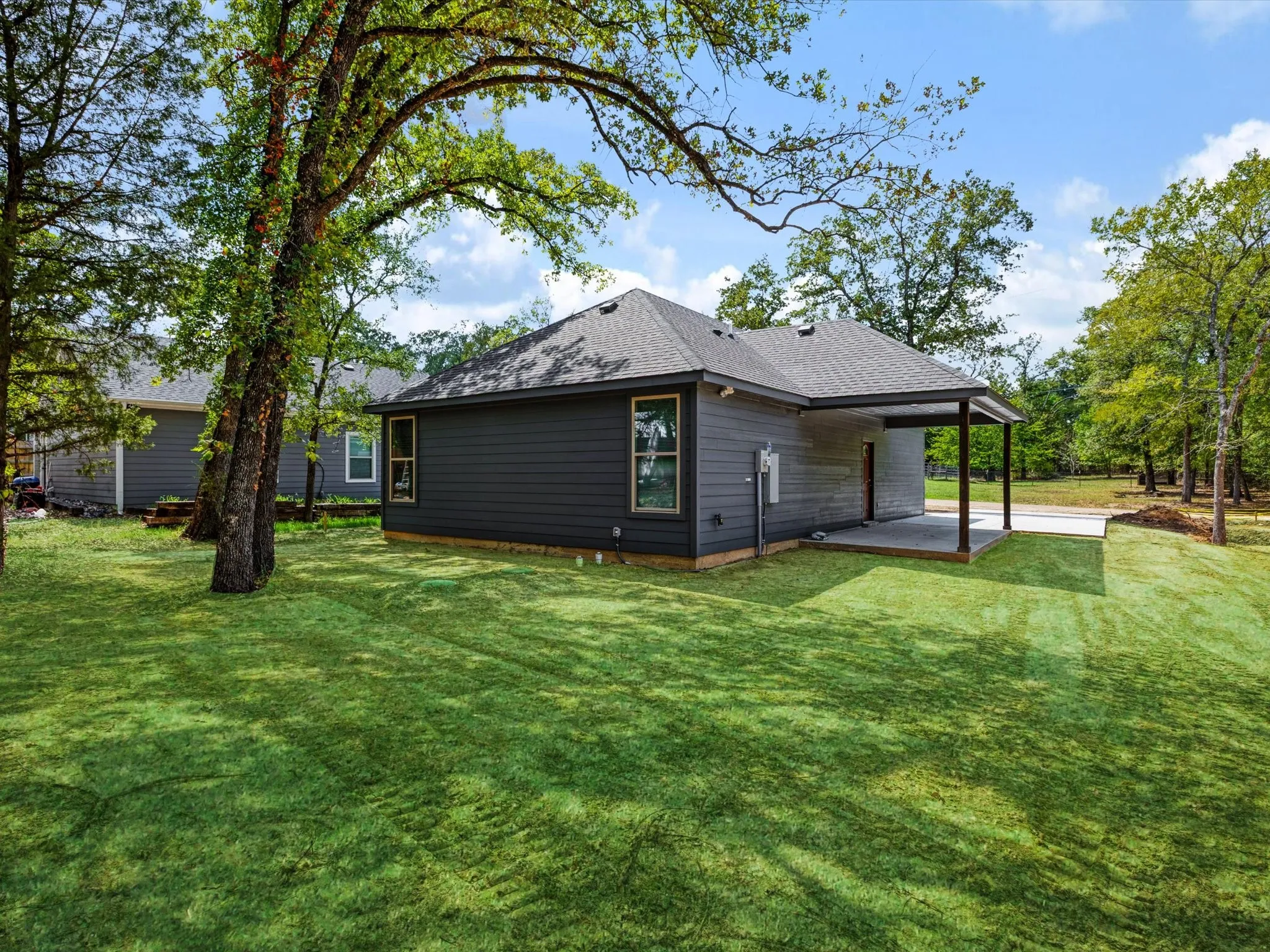 Expansive backyard featuring a manicured lawn, mature trees, and a covered patio