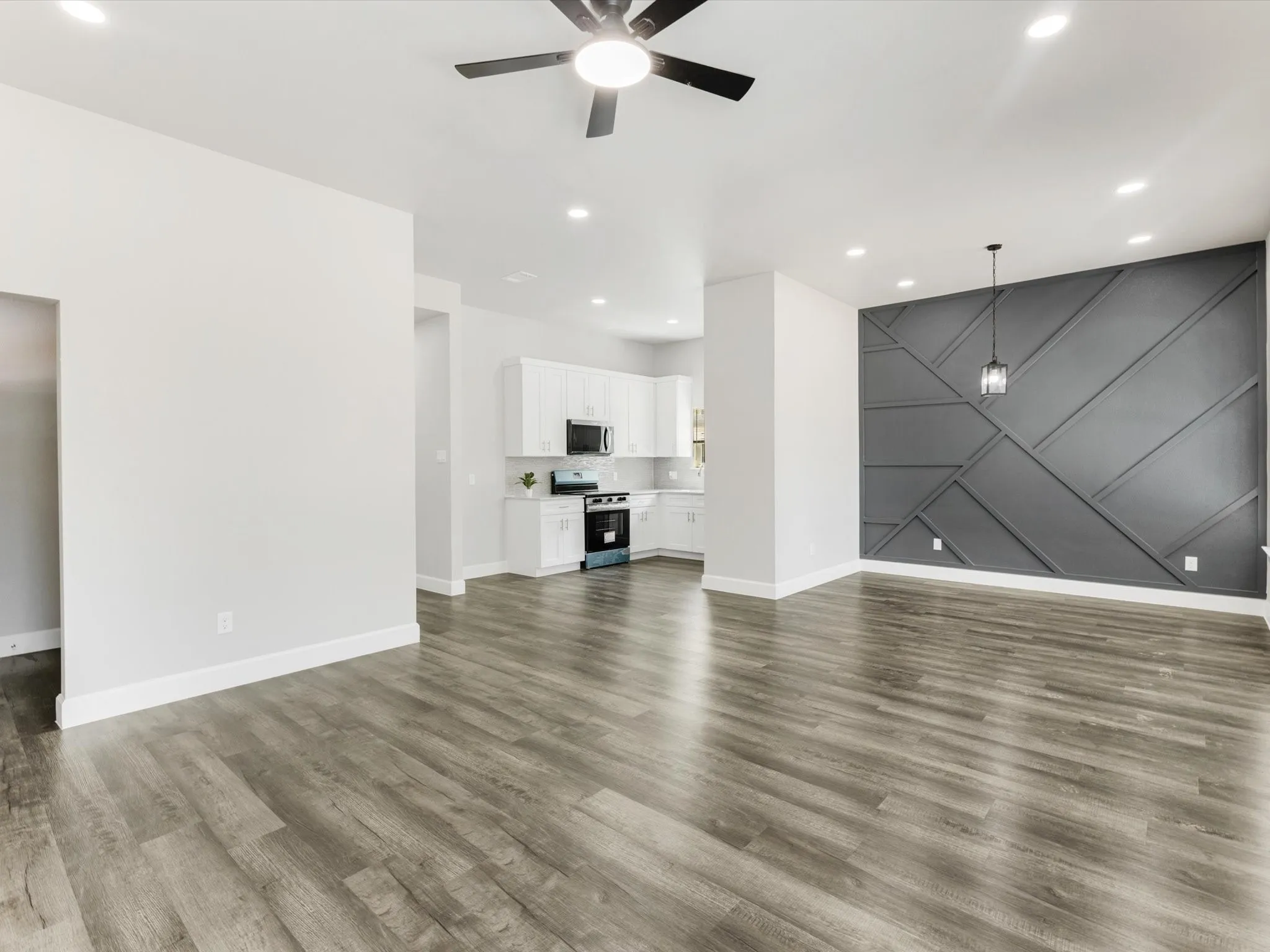 Open-concept living space with wood-finish flooring, recessed lighting, ceiling fan, and a decorative accent wall