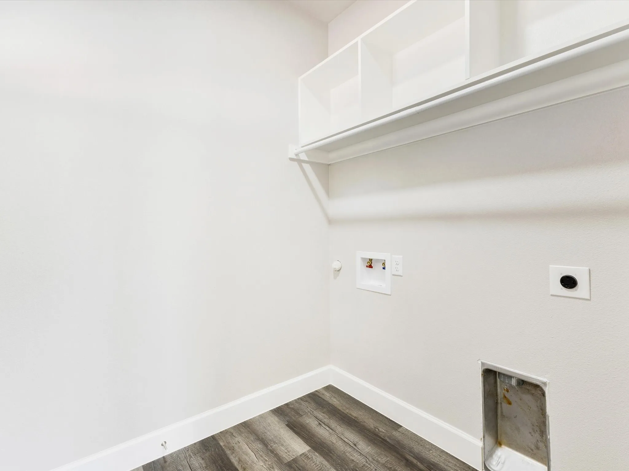 Utility area featuring built-in shelving, a clothes rod, wood-finish flooring, and white baseboards