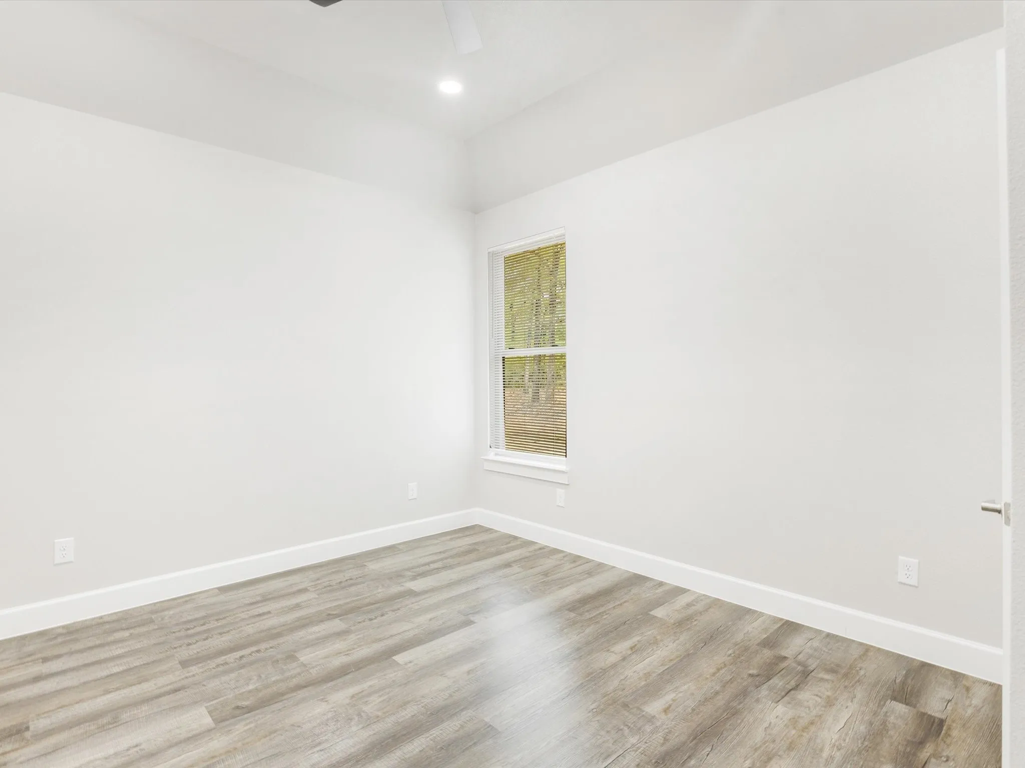 Vaulted ceiling with a recessed light fixture, a single window, and wood-finish flooring